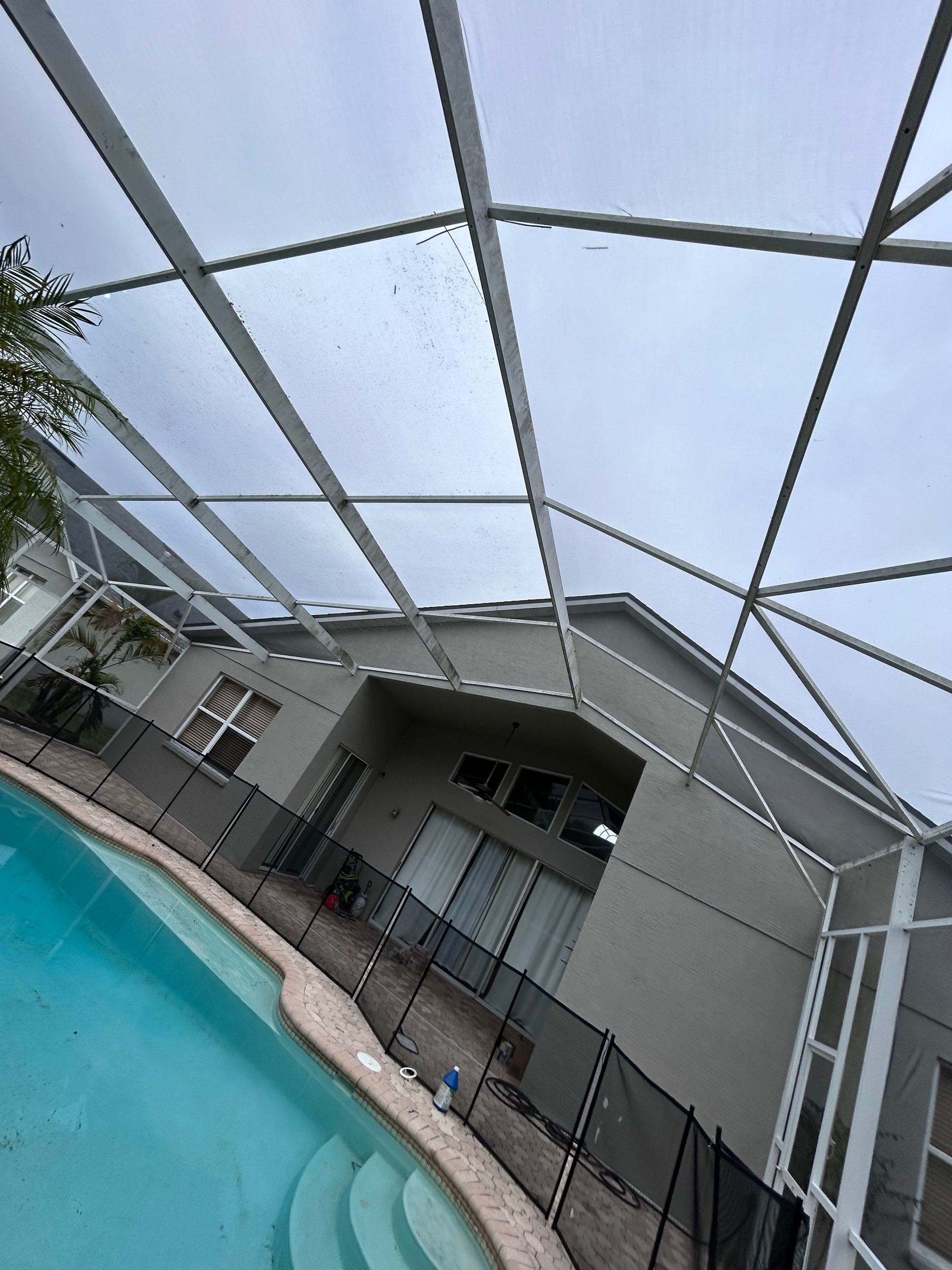 A pool with a screen enclosure next to a light gray house under a cloudy sky.