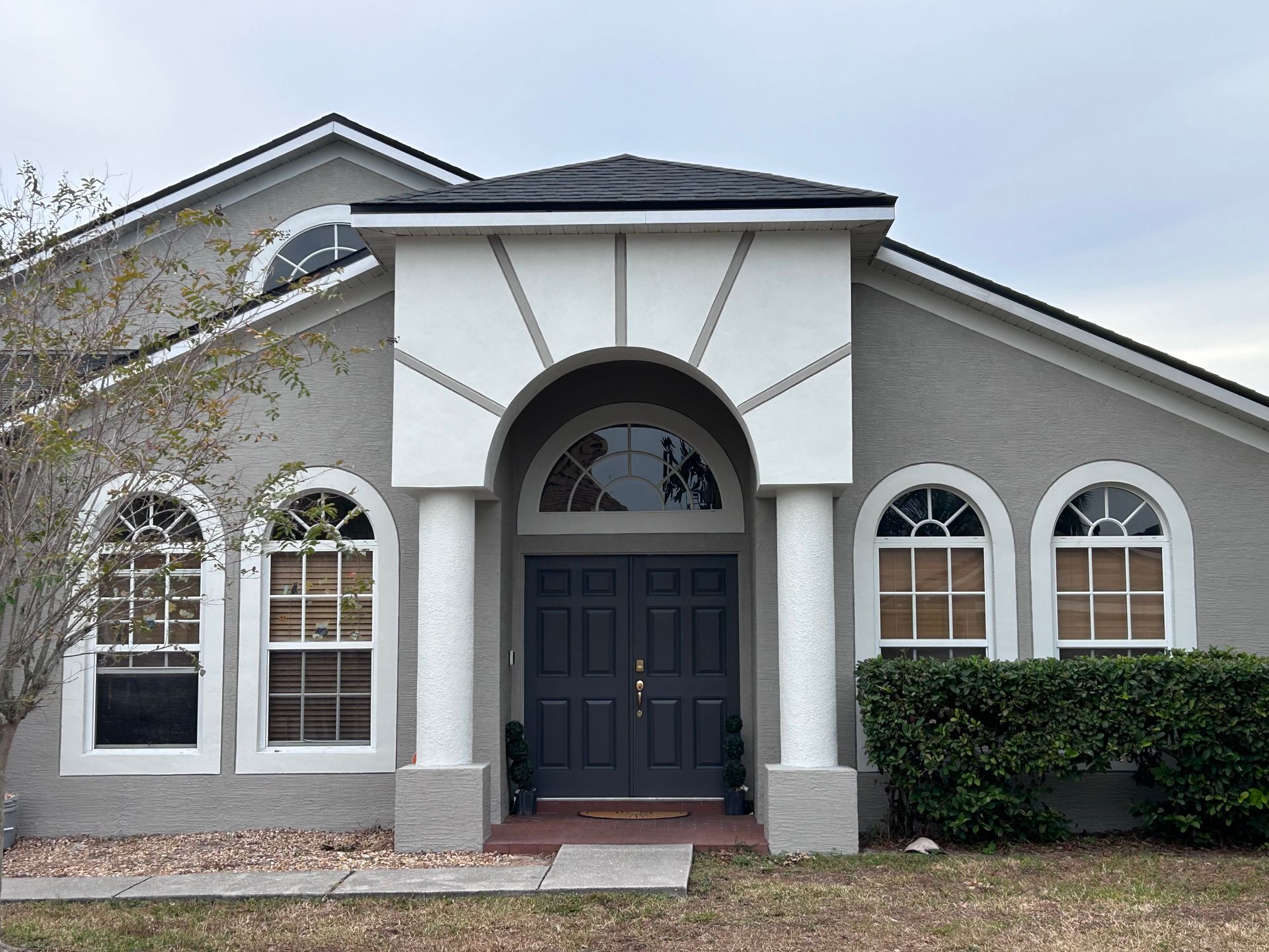Gray stucco house with arched windows and a dark double door entrance.