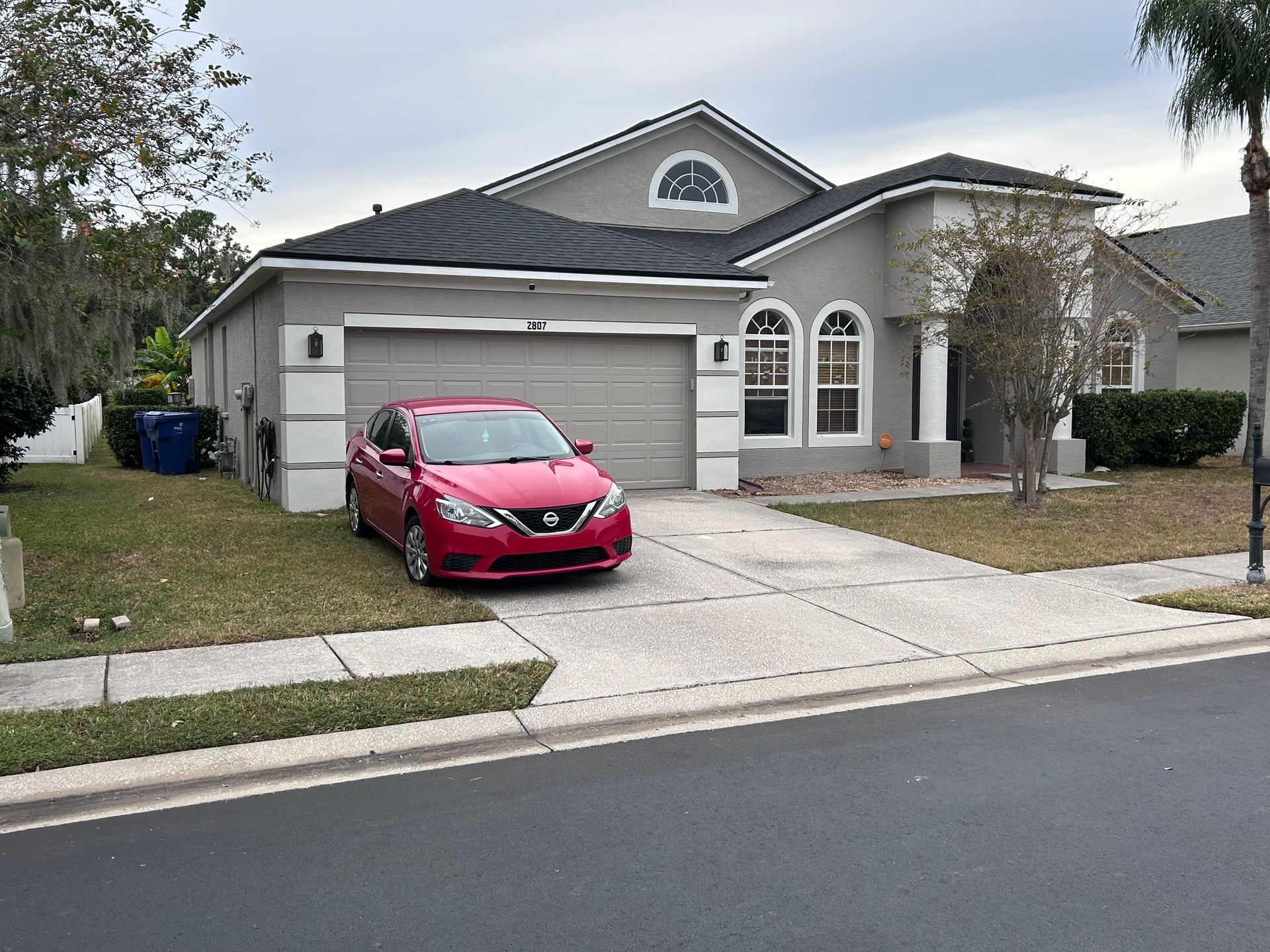 Red car parked in front of a gray house with a two-car garage. Overcast day.