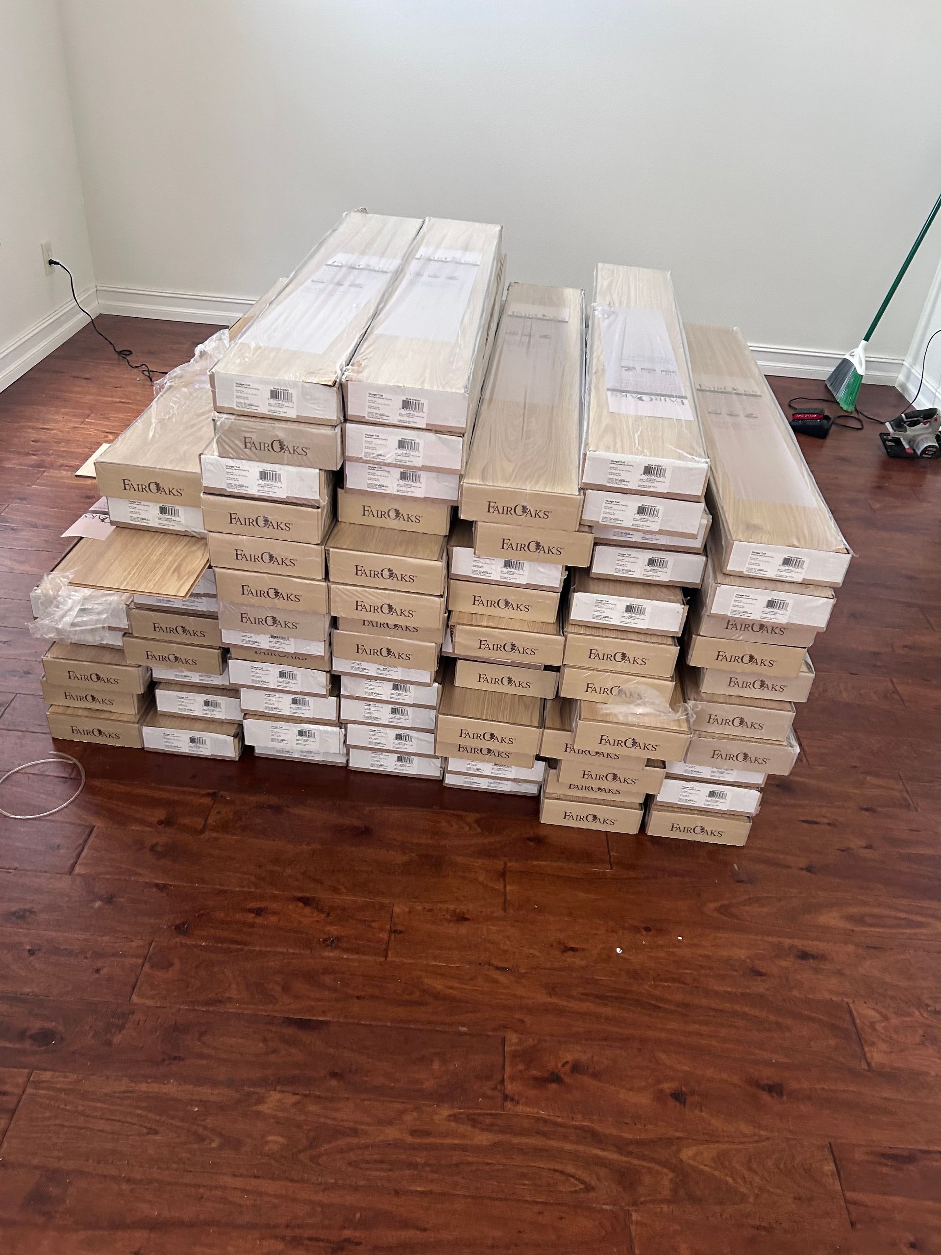 Pile of boxed wooden flooring on top of existing wood floor in a room.