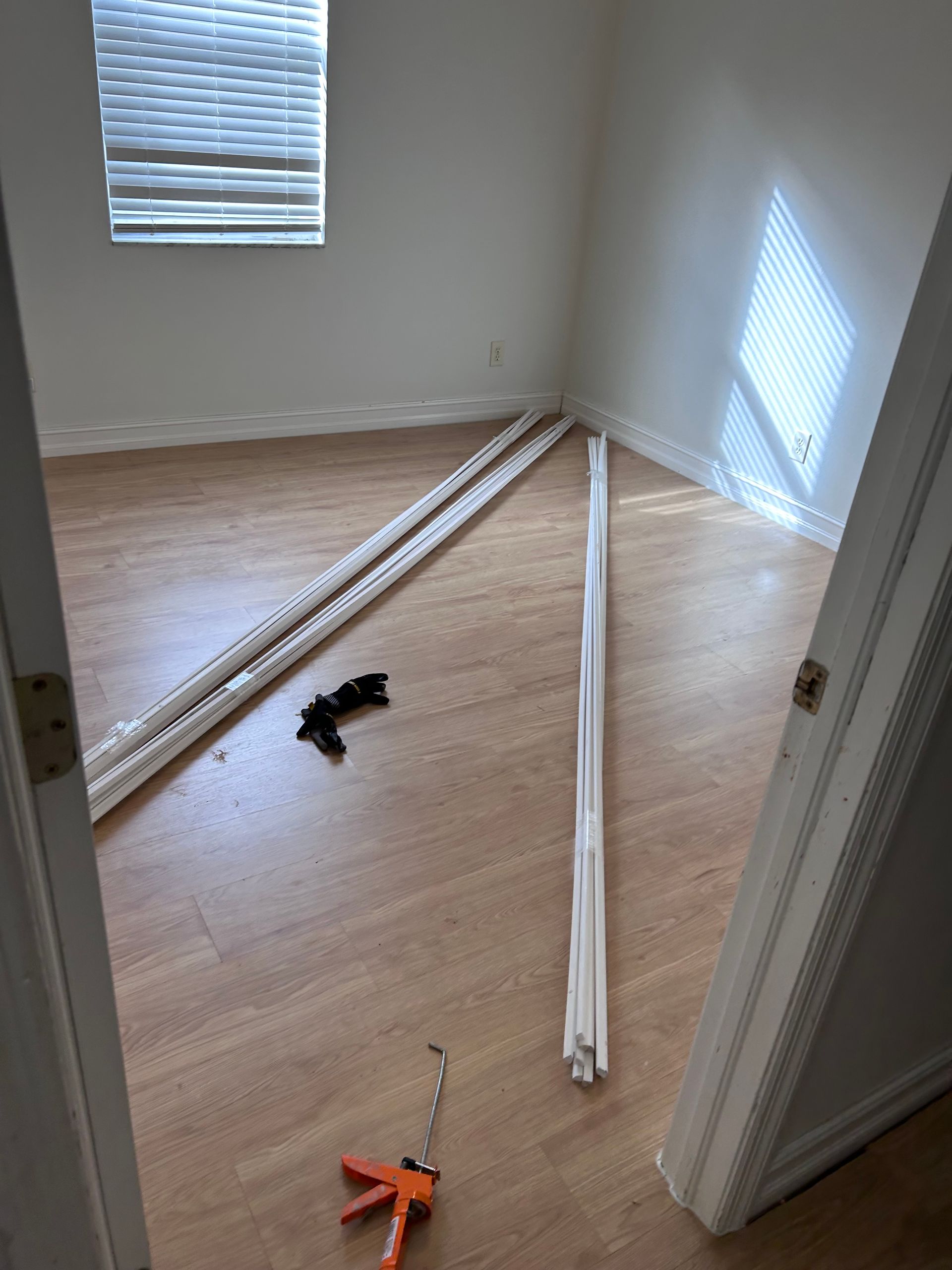 Room interior with trim pieces on floor, caulking gun, and window with blinds.