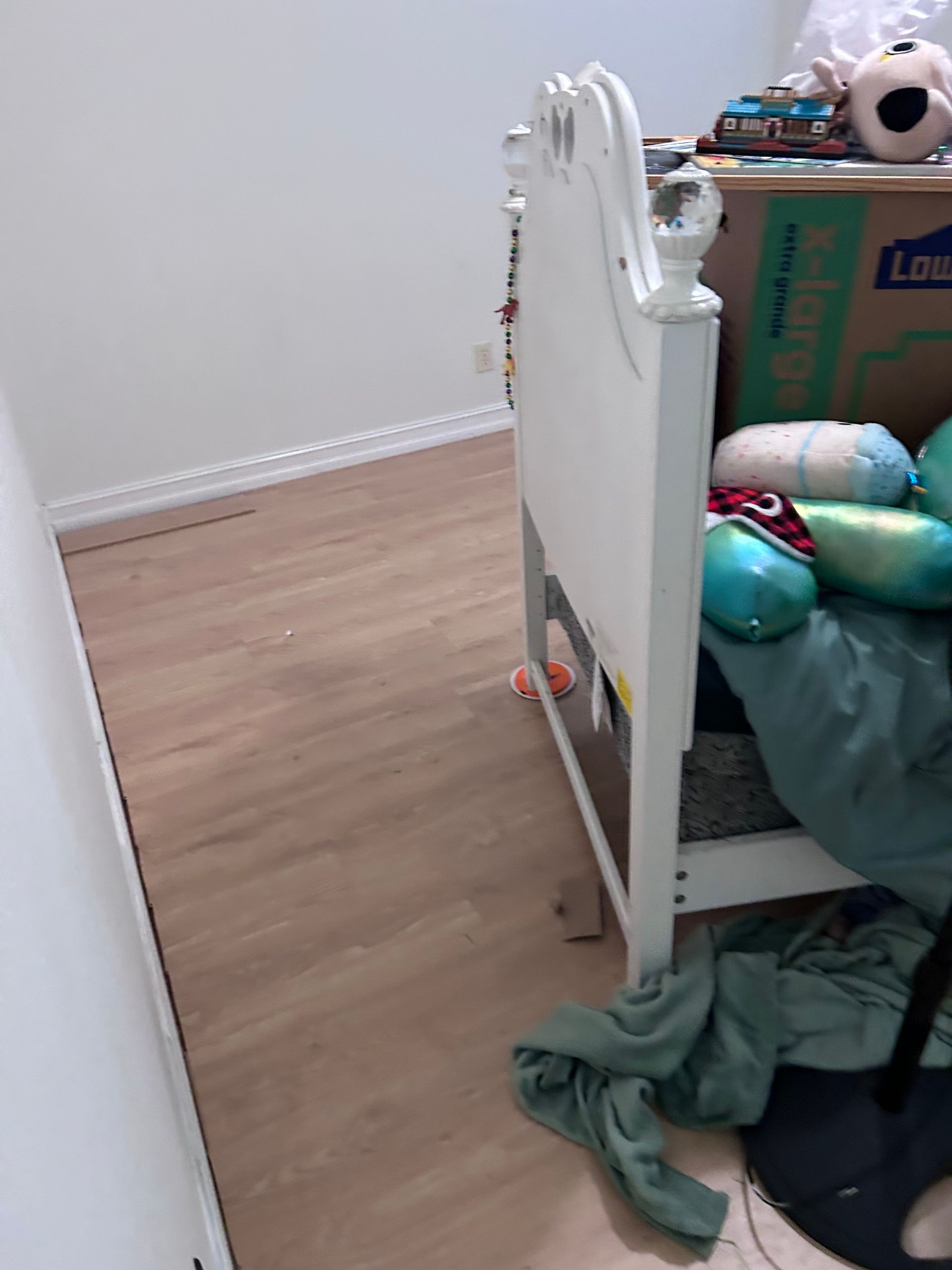 White headboard next to a box and bed with scattered objects on a wooden floor.