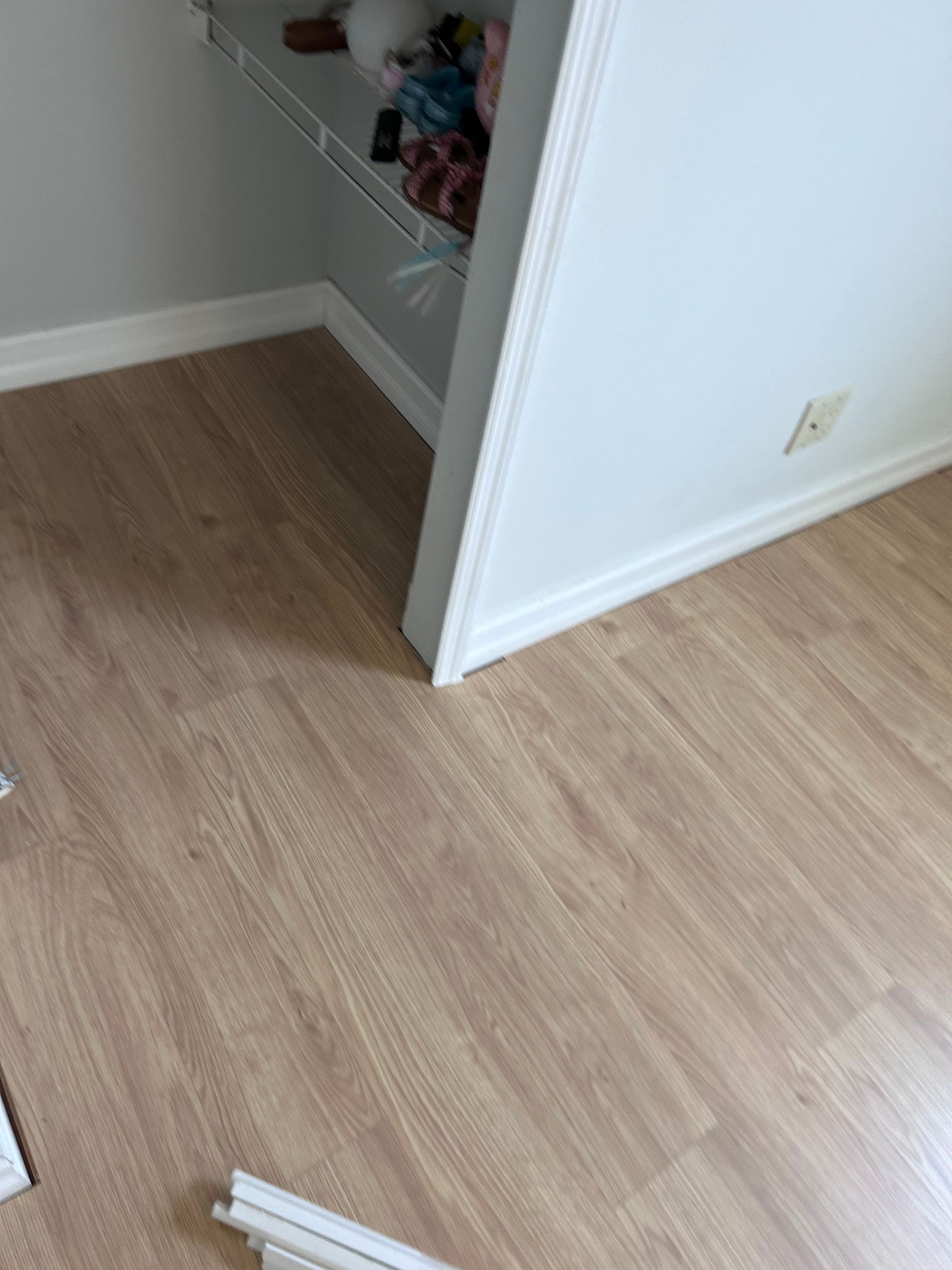Light wood-look flooring installed in a room, meeting a doorframe with white trim.