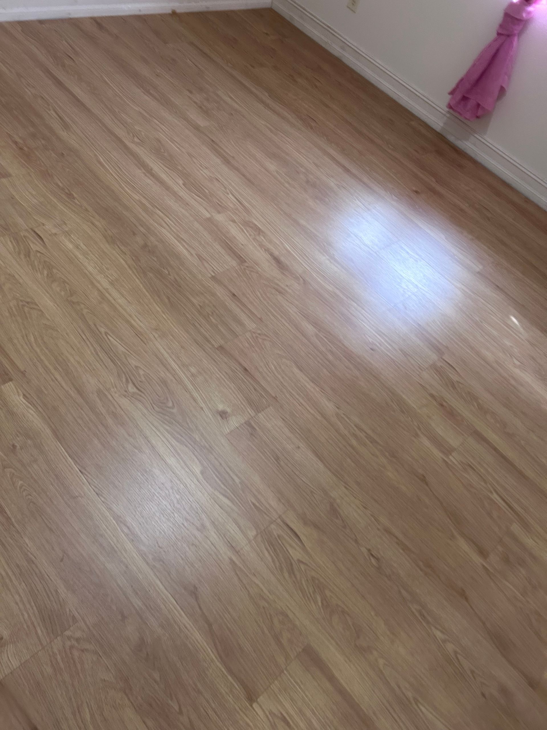 Light brown laminate flooring in a room with a white wall and a pink curtain.