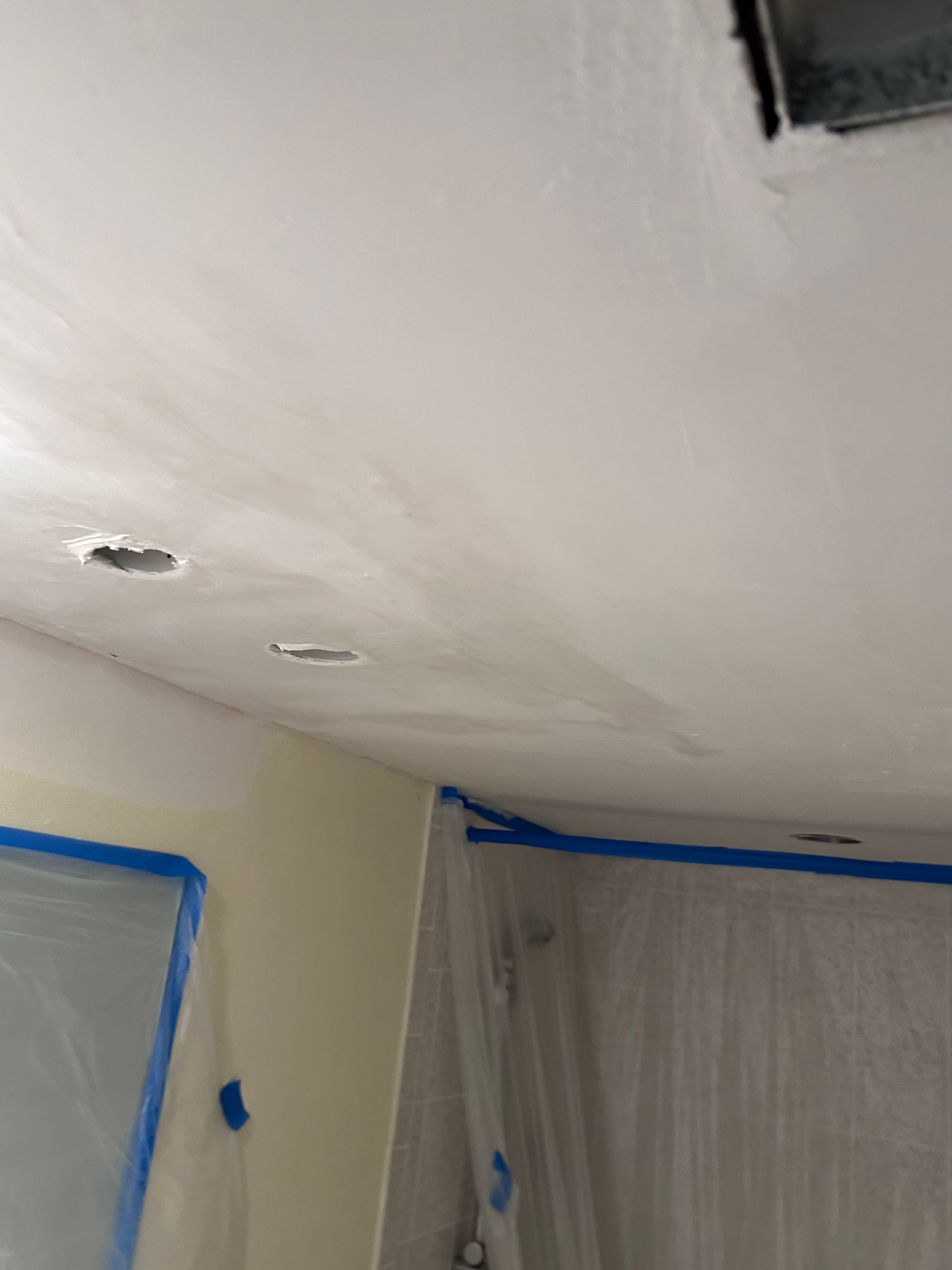 White ceiling and wall being painted, blue tape along edges, recessed lights.