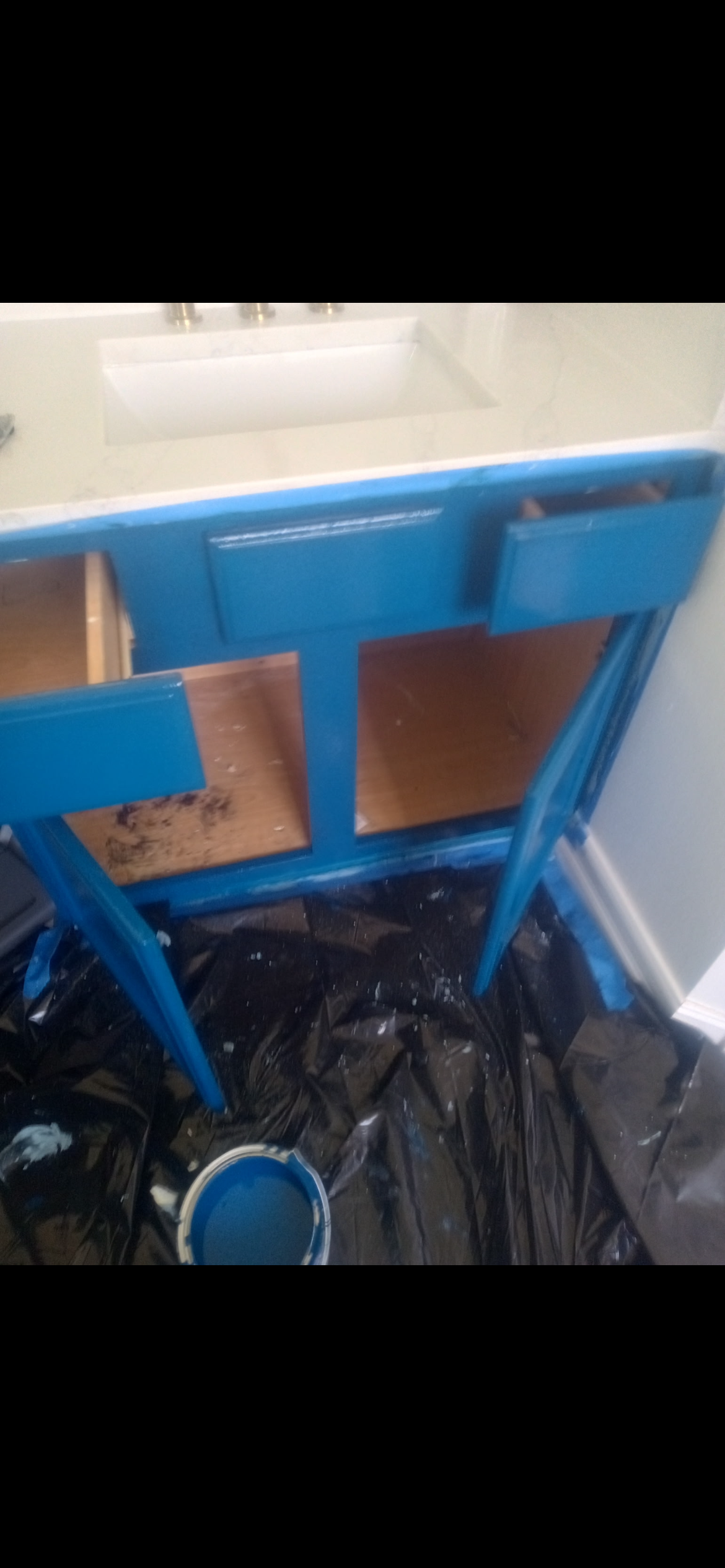 A blue painted desk with drawers, sitting on black plastic, with a paint can visible.