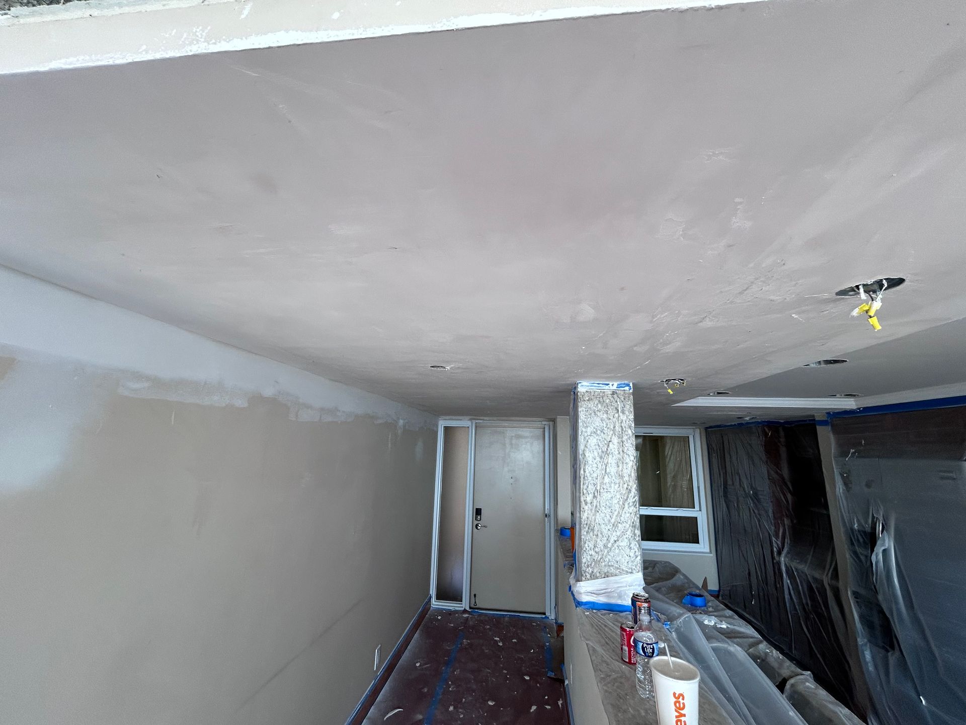 Renovated interior: drywall ceiling and wall, doorway, covered objects, paint cans, and window.