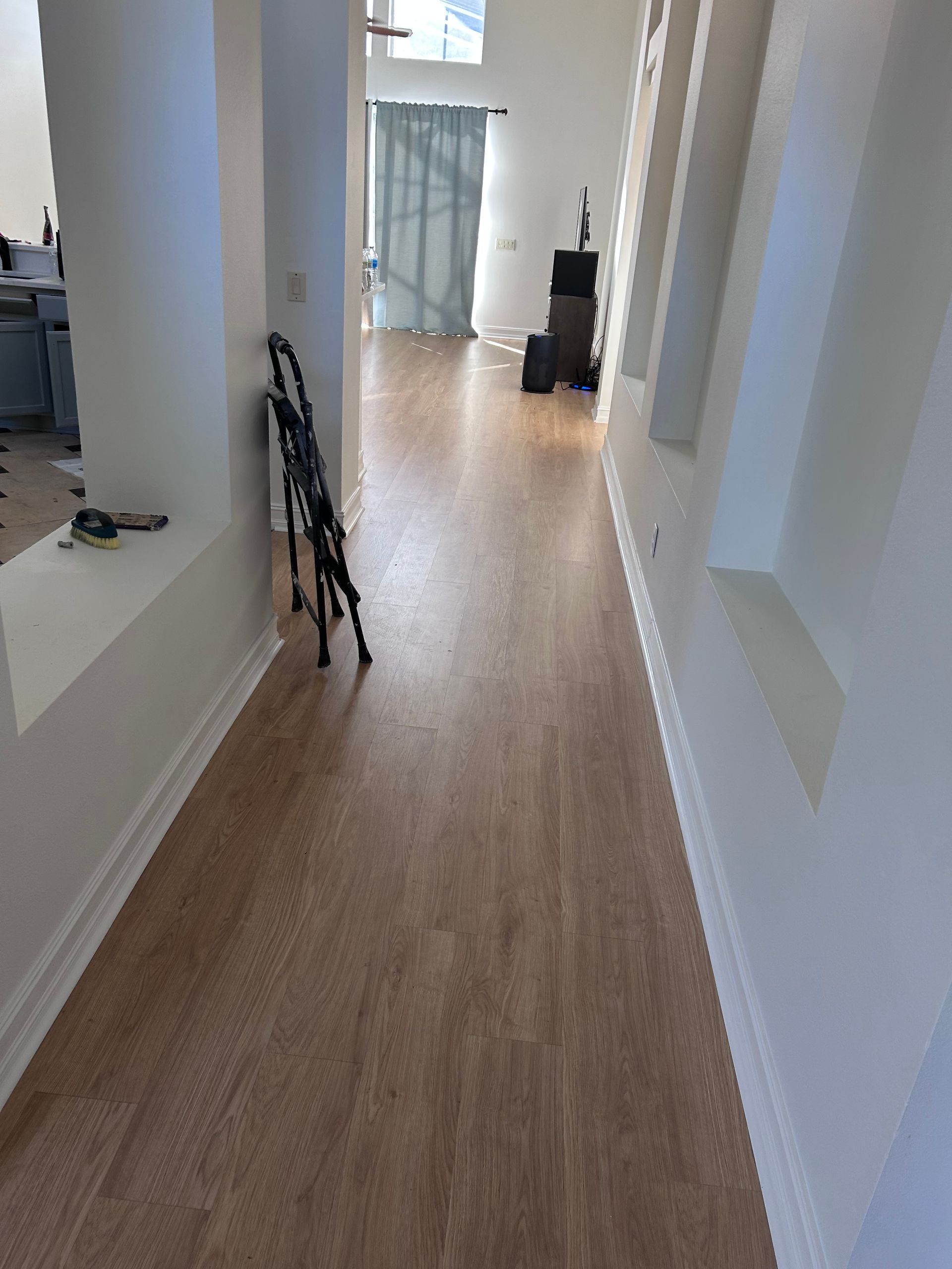 Long, light-brown wood-floored hallway with white walls and architectural niches. A folded black object sits in the middle.