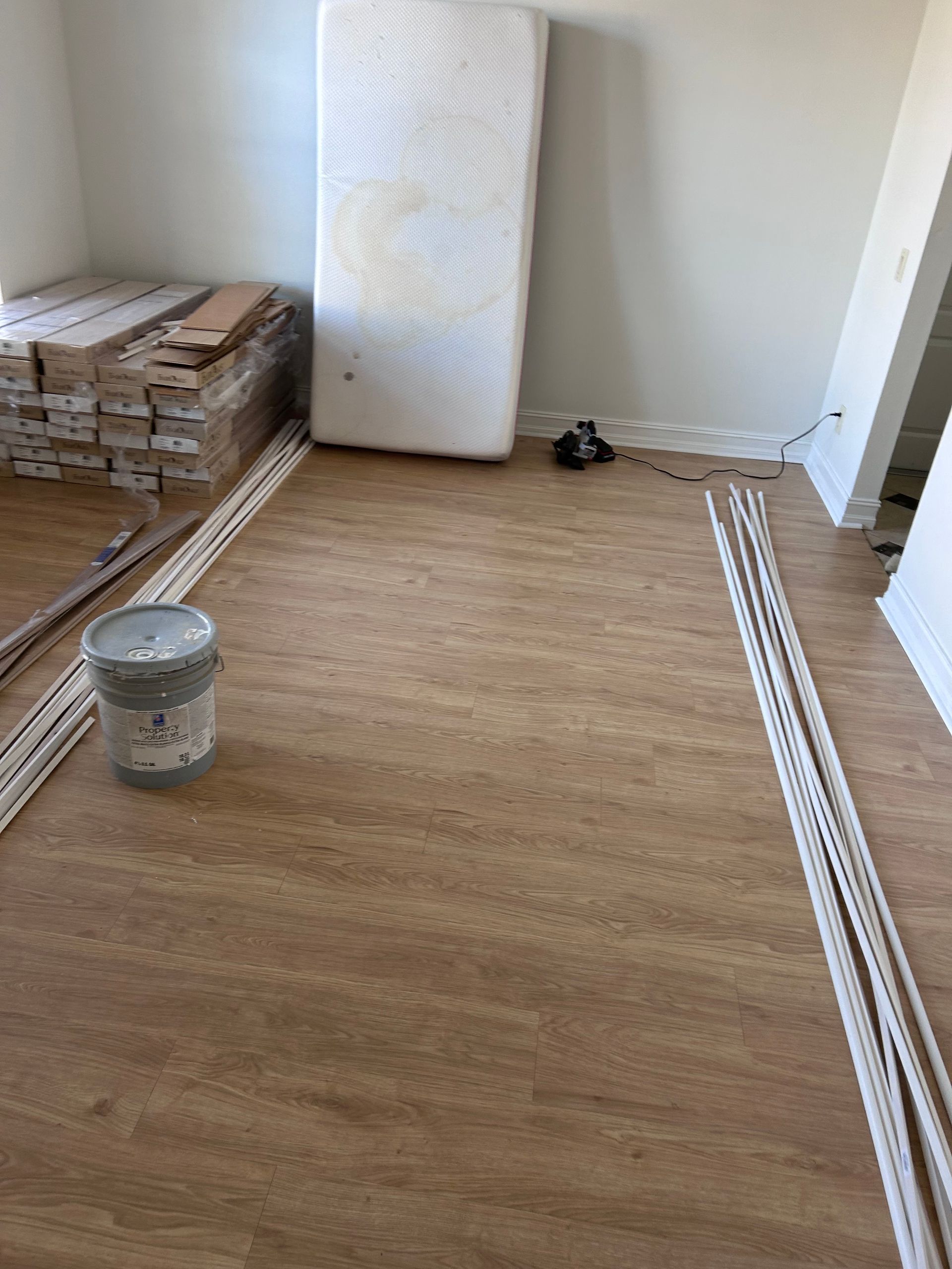 Room under construction with new flooring installed. Materials and a mattress are present.