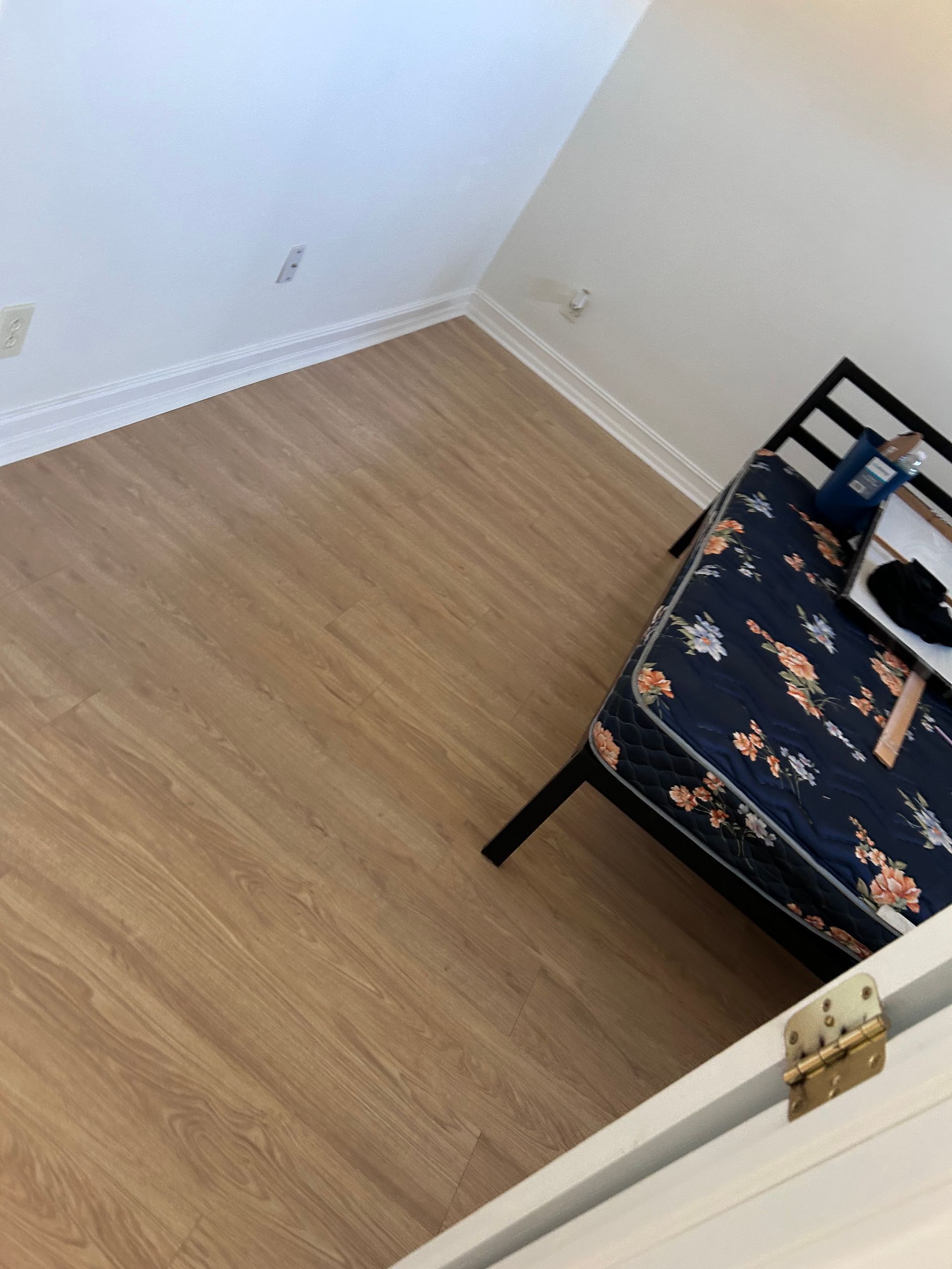 Bedroom with wood-look flooring and a metal-framed bed with floral bedding. White walls and trim.