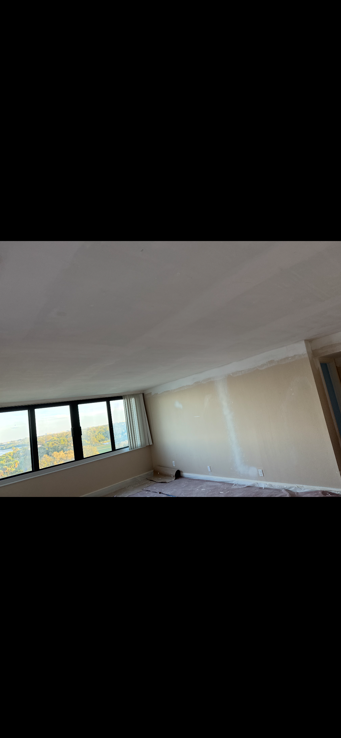 Empty room with large windows, neutral walls, and a view of the outside.