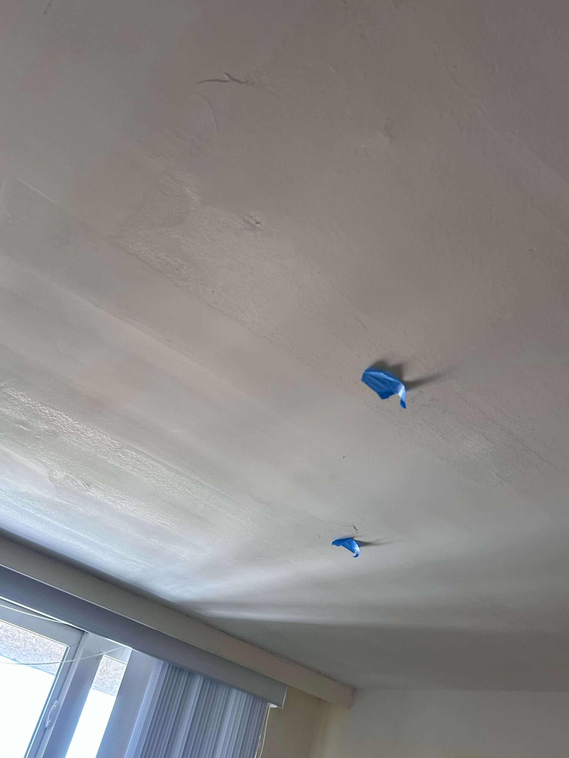 White ceiling with blue tape, likely indicating a repair or painting project near a window with curtains.
