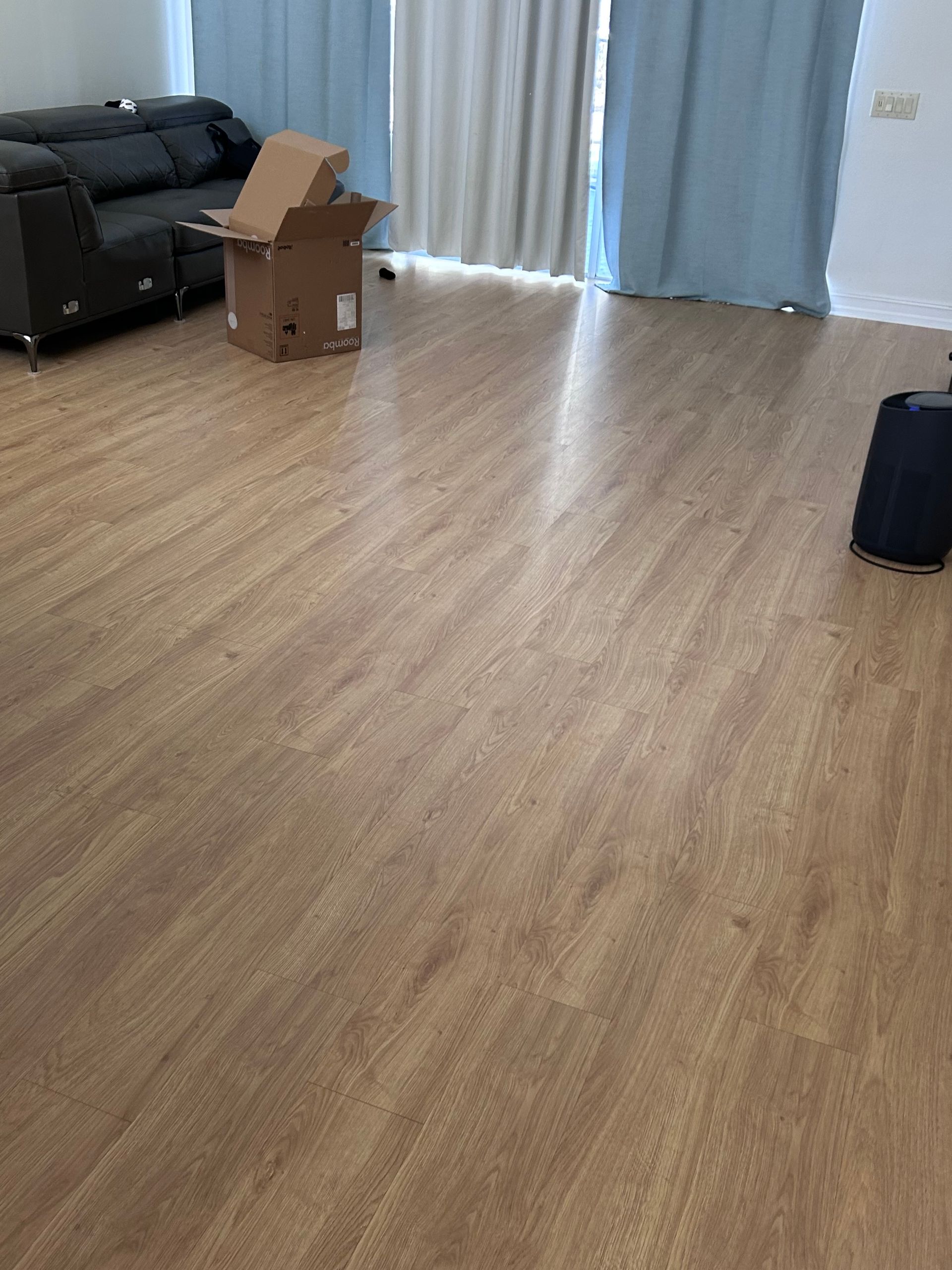 Wooden floor in a room with a sofa, cardboard box, and curtains.