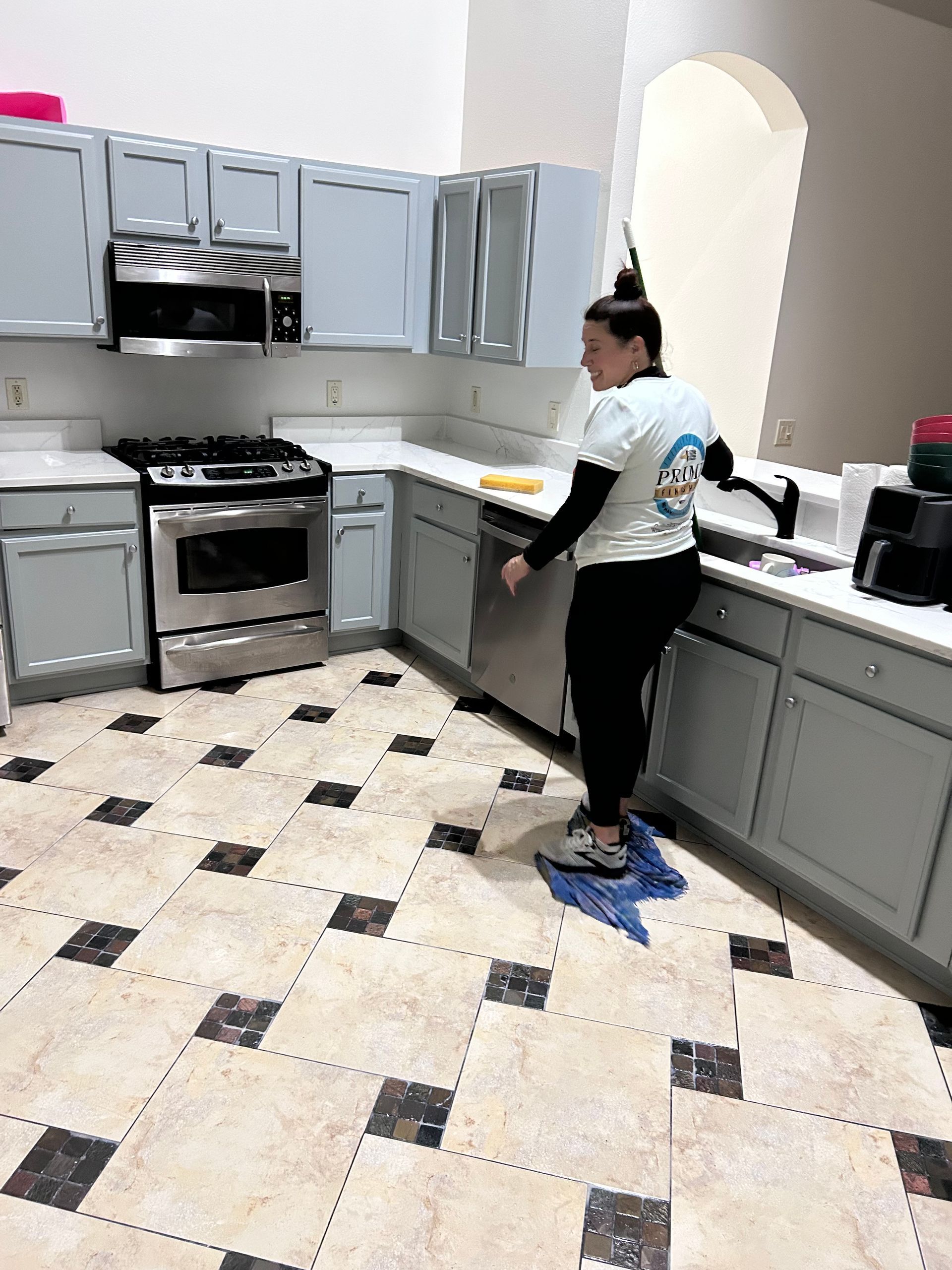 Woman in kitchen with gray cabinets and stainless steel appliances.