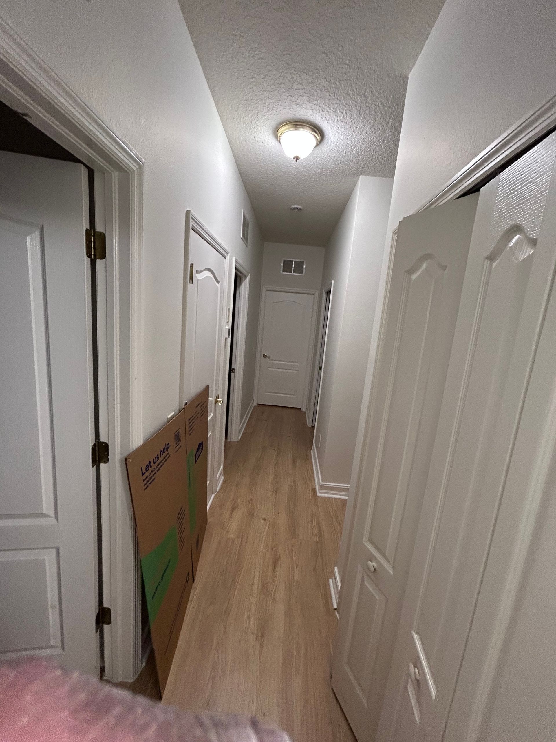 Narrow hallway with doors, cardboard box, and a light fixture.