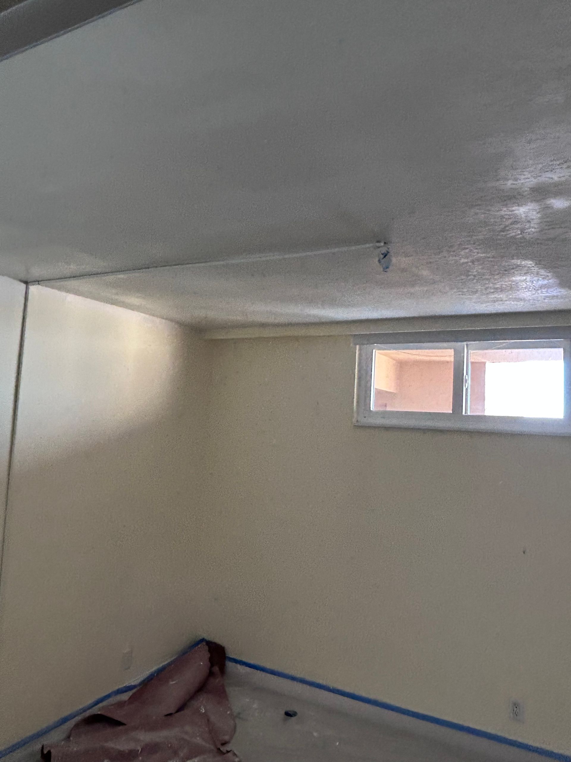 Interior view of a room with off-white walls, a window, and a textured ceiling.