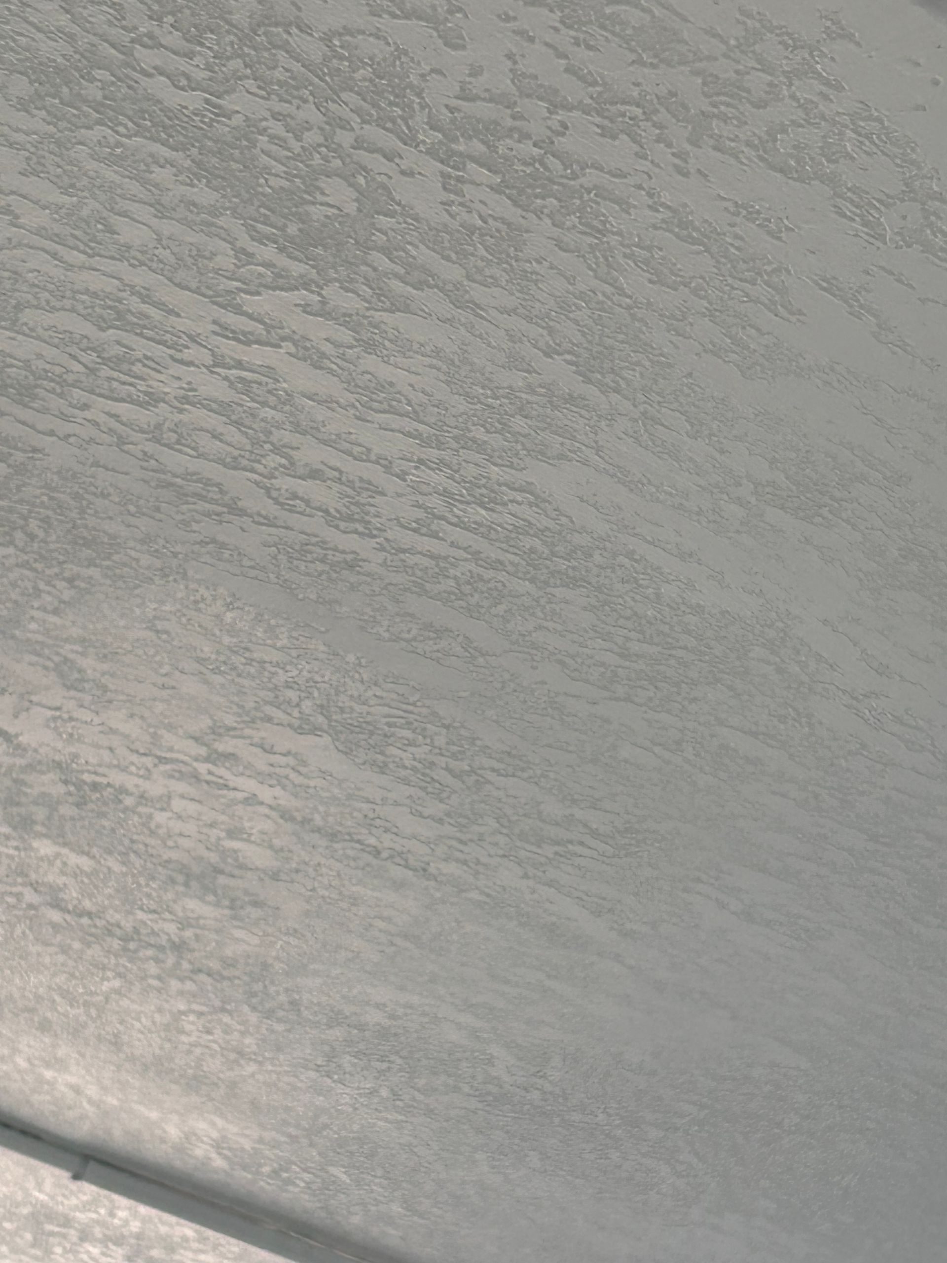 Close-up of a textured, light gray surface, possibly a ceiling, with varying patterns.