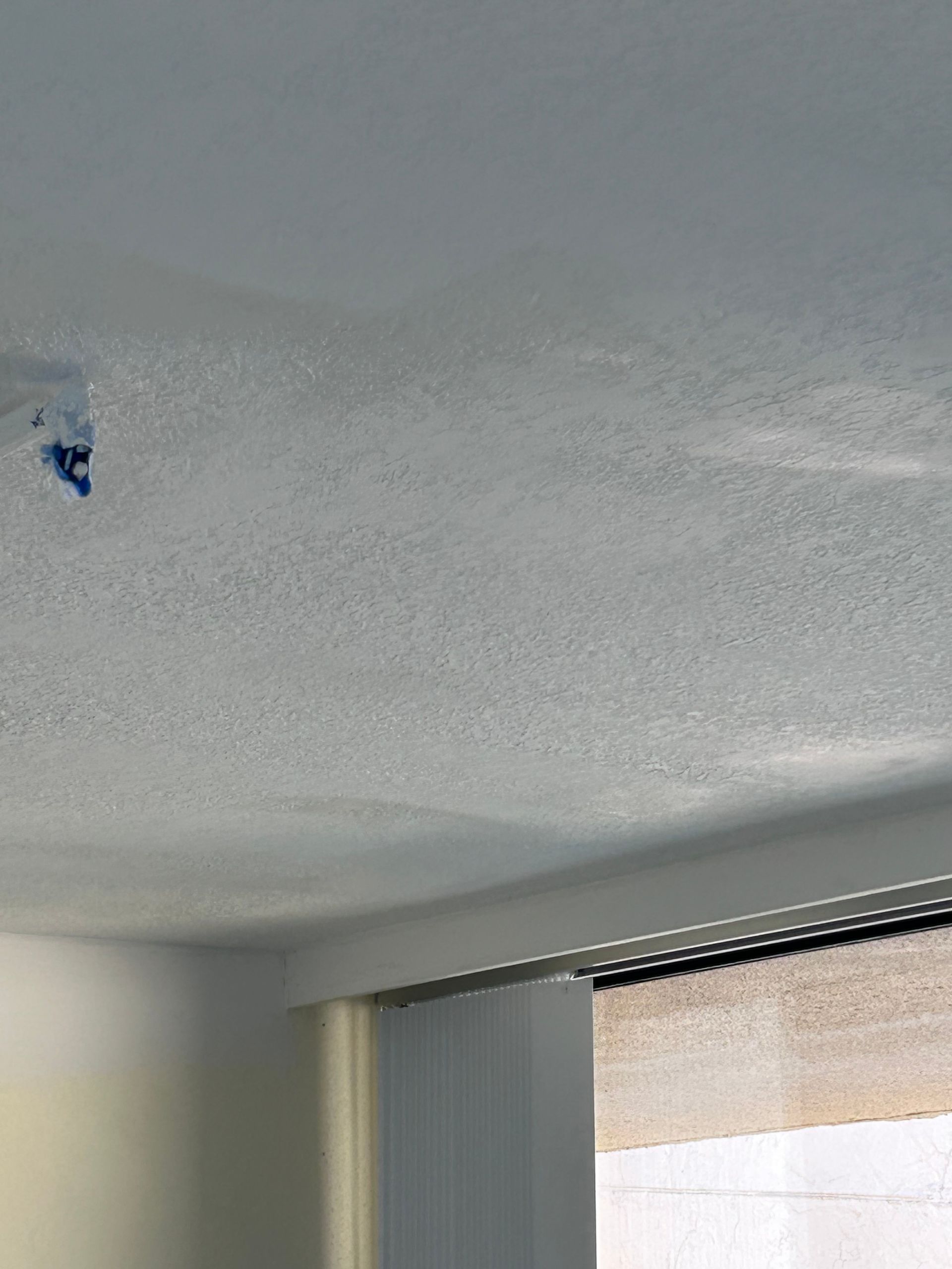 Textured white ceiling with a dark blue stain and a partially visible window.