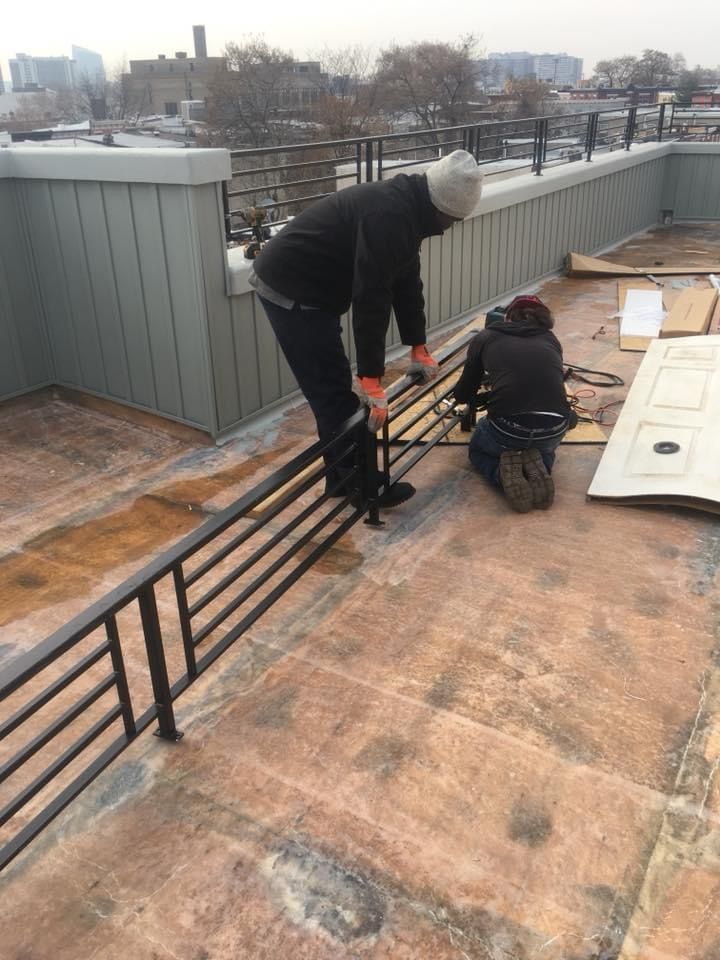 Two men are working on a railing on a roof.