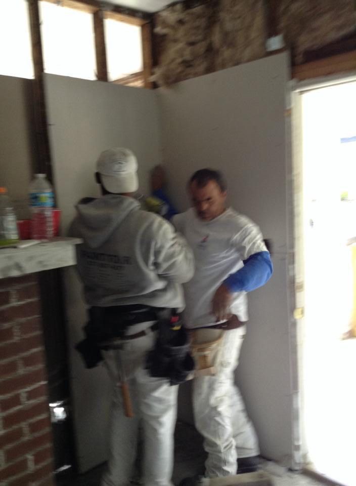 Two men are working on a wall in a room