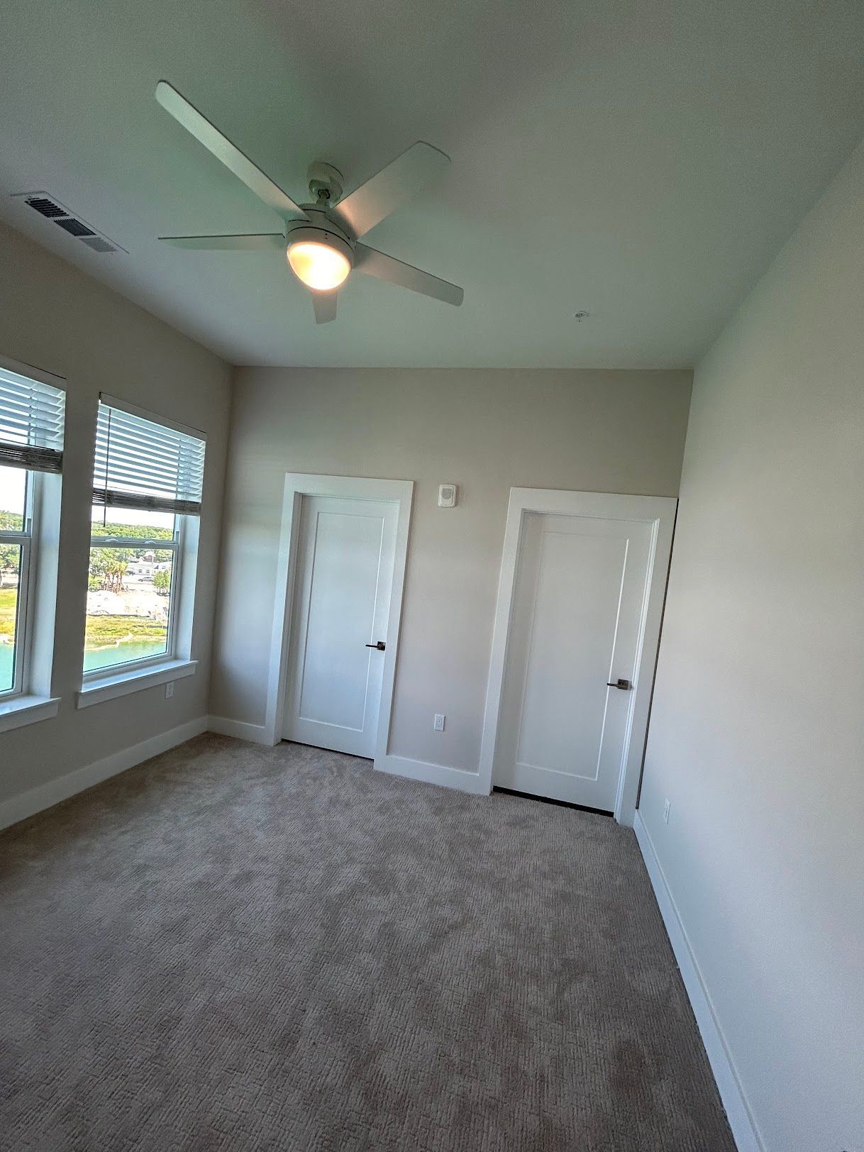 An empty bedroom with a ceiling fan and two windows.