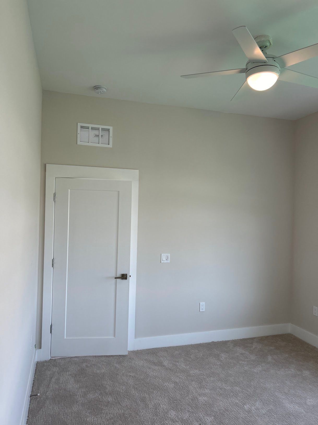 An empty bedroom with a ceiling fan and a door.