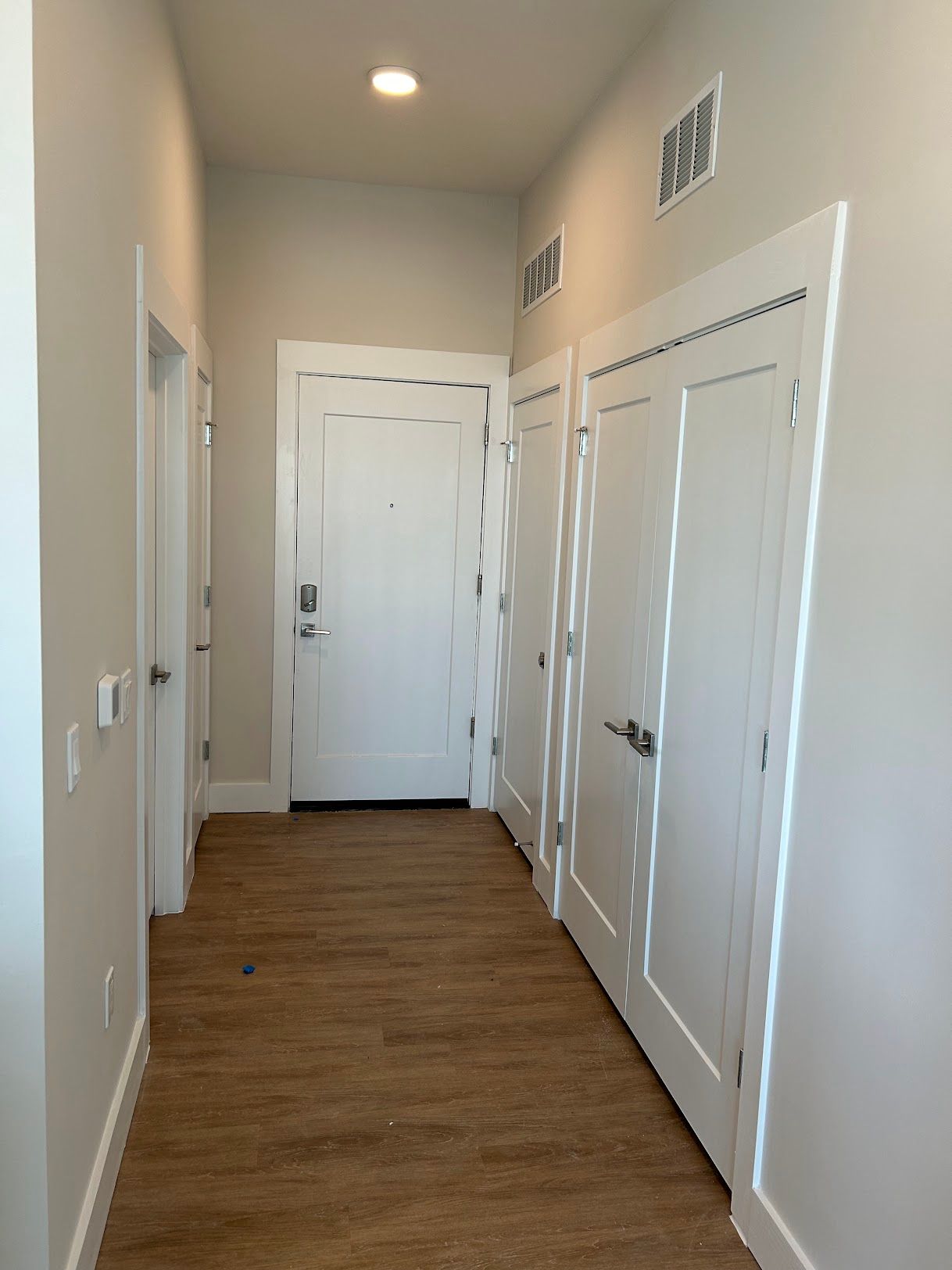 A long hallway with wooden floors and white doors leading to a door.