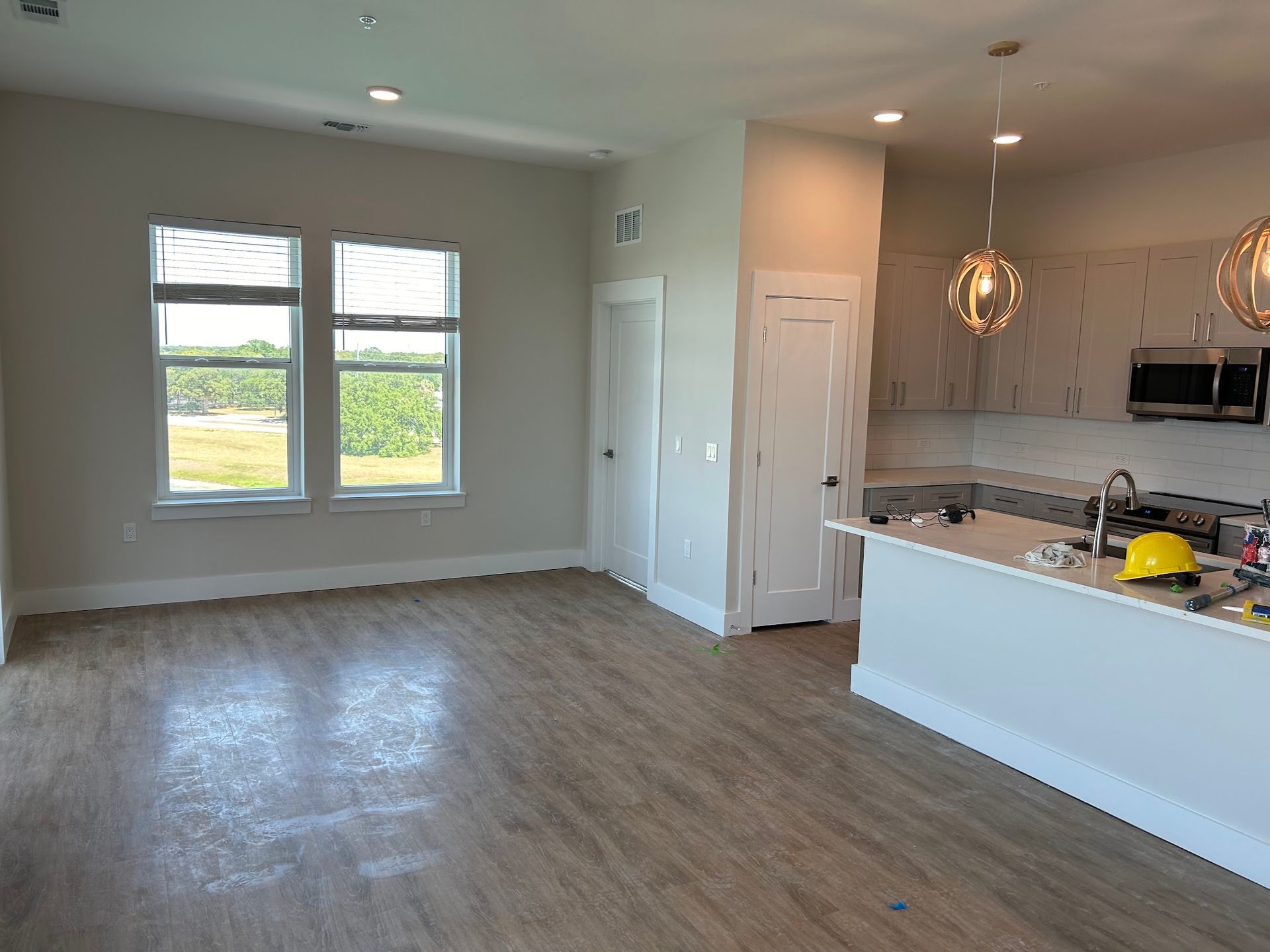 An empty living room with hardwood floors and a kitchen in the background.