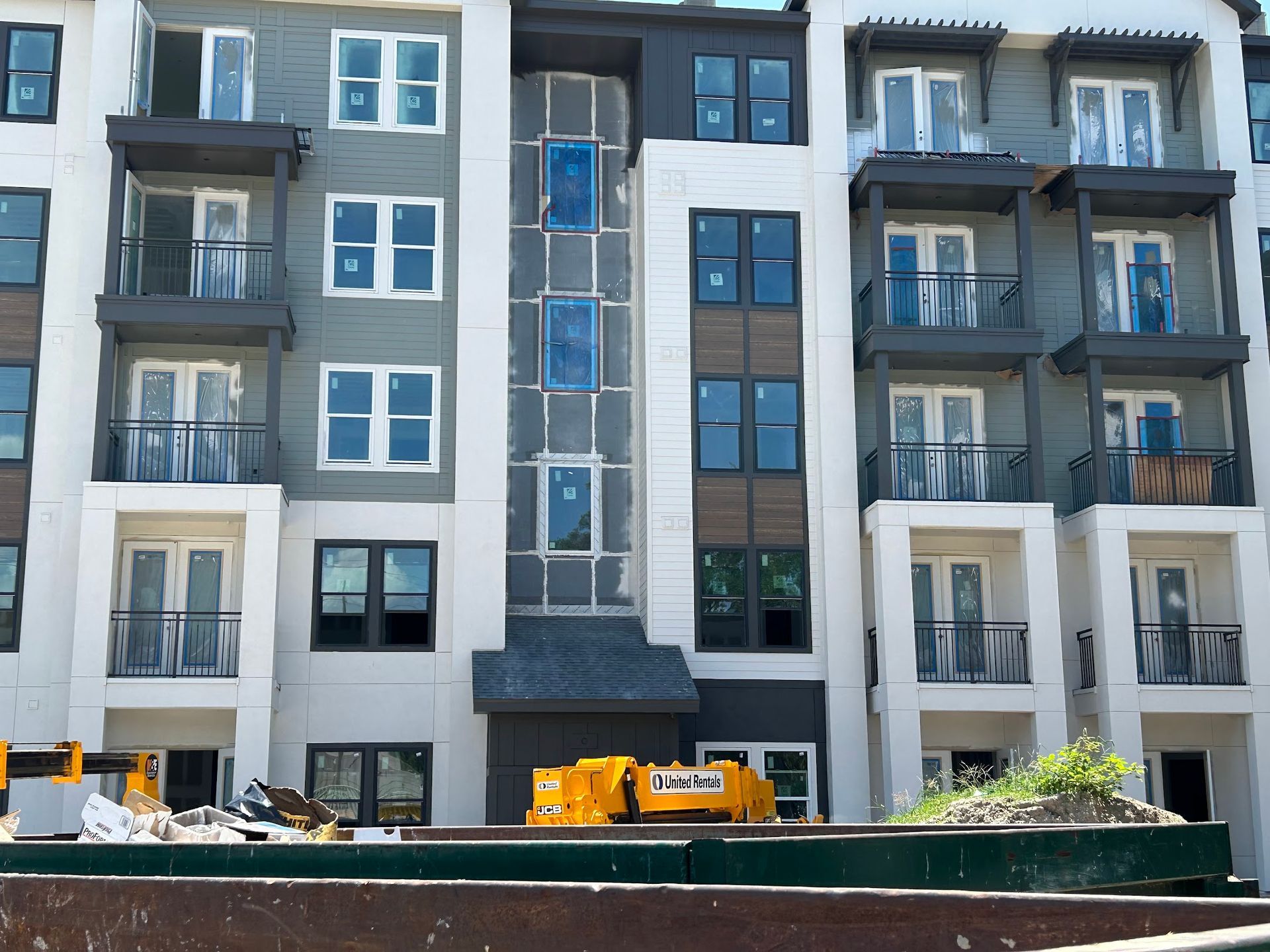 A large apartment building under construction with a yellow dumpster in front of it