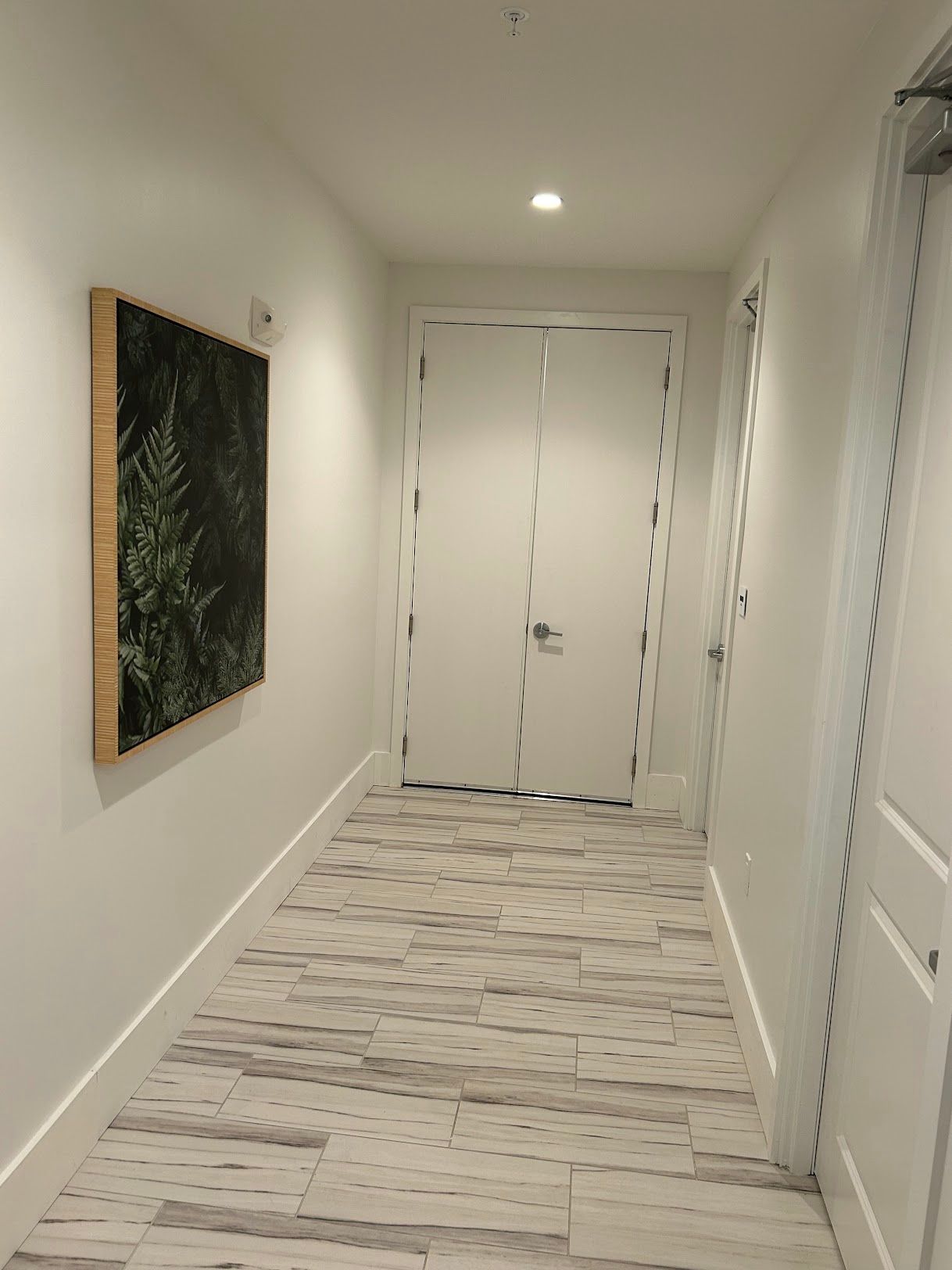 A long hallway with a picture on the wall and a wooden floor.