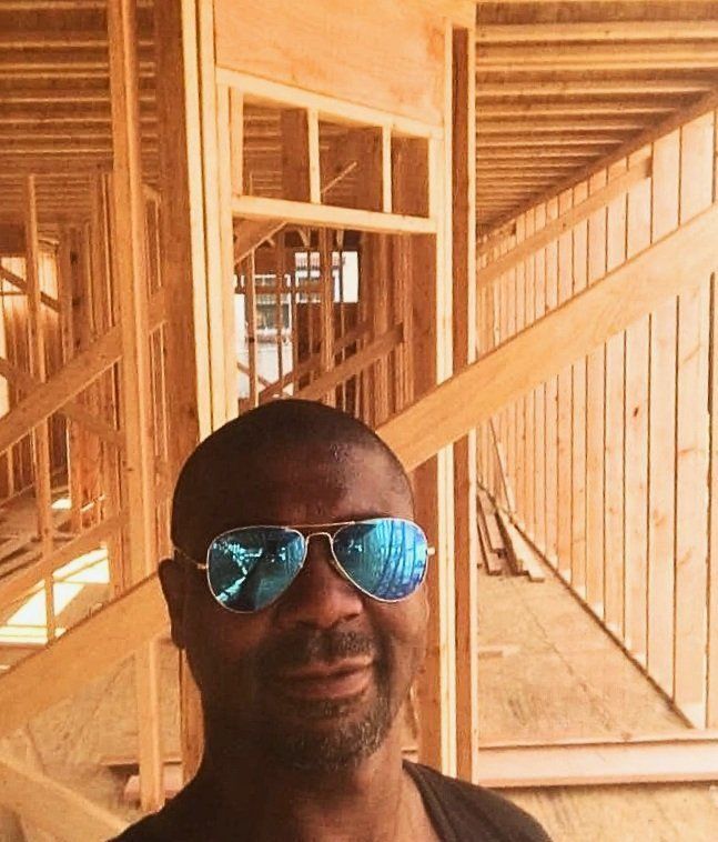 A man wearing sunglasses is standing in front of a building under construction