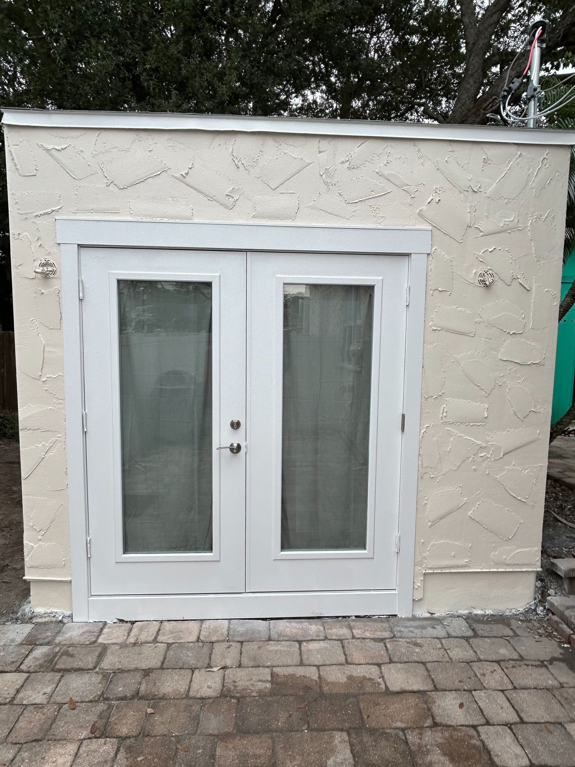 A white building with two white doors on a brick patio.