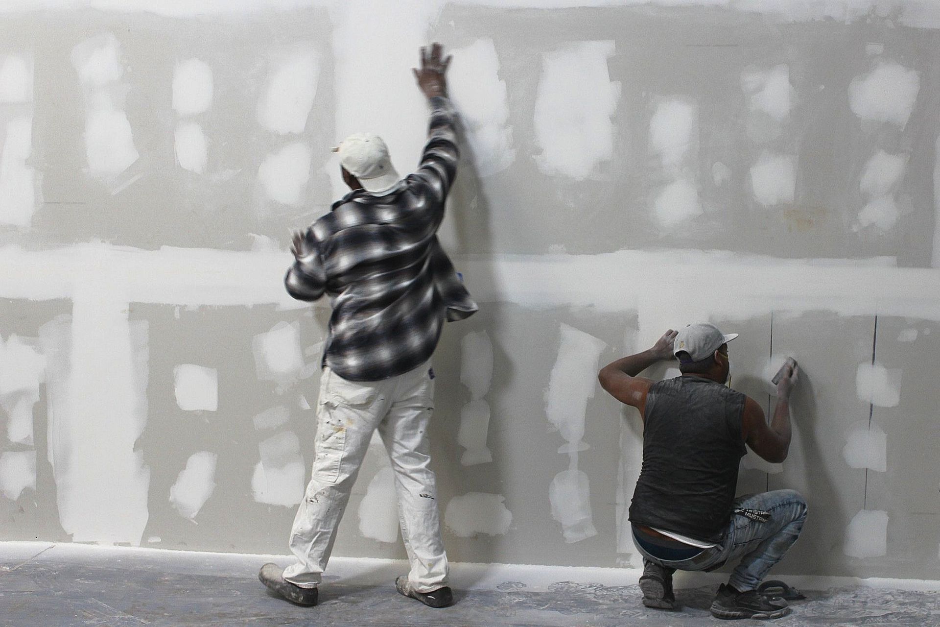 Two men are working on a drywall wall.