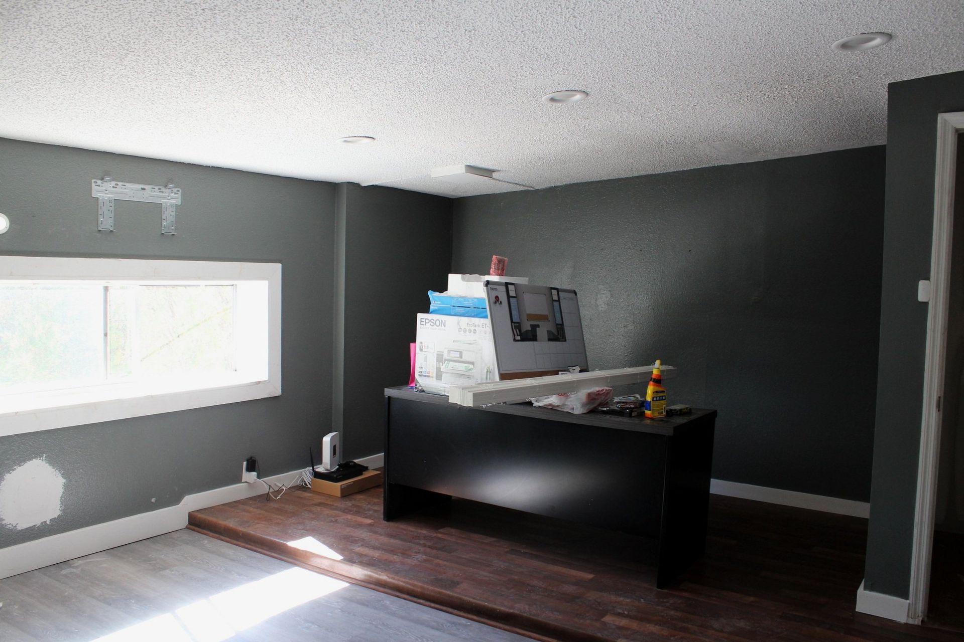 A room with gray walls and a black desk in it.