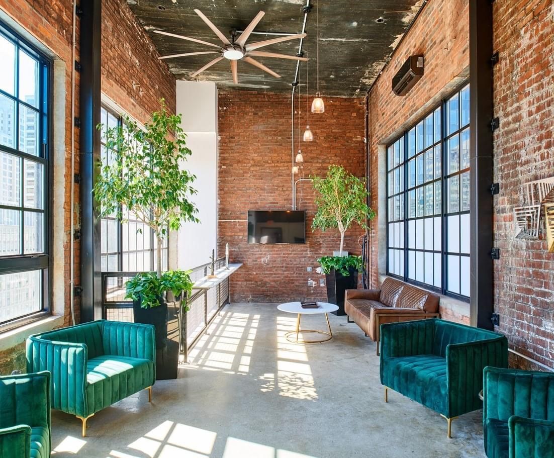 A living room with green chairs , a couch , a table and a ceiling fan.