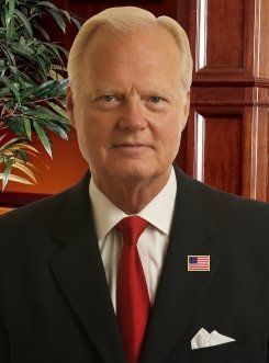 A man in a suit and tie is standing in front of a plant.