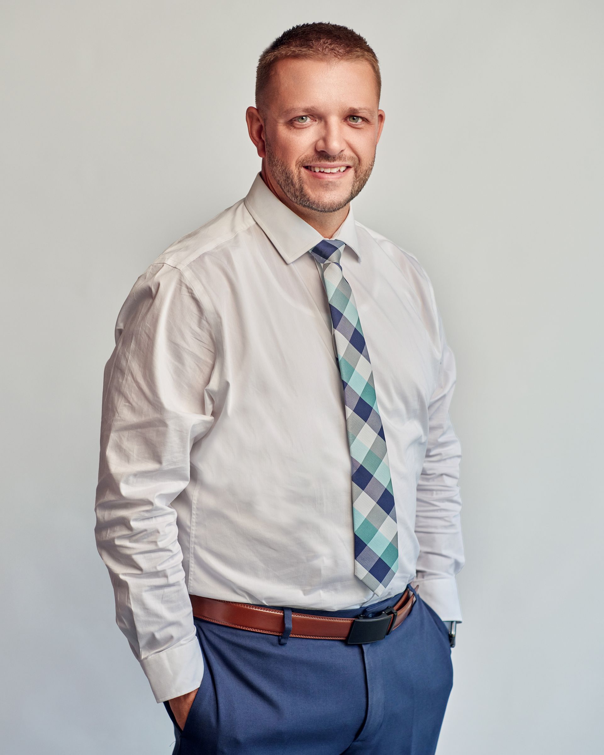 A man in a white shirt and tie is standing with his hands in his pockets.