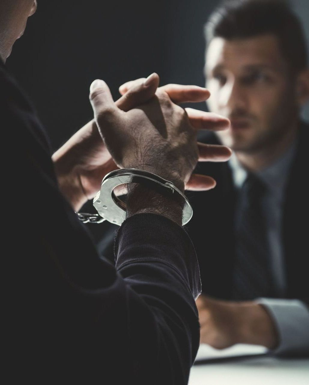 A man in handcuffs is talking to another man in a suit.