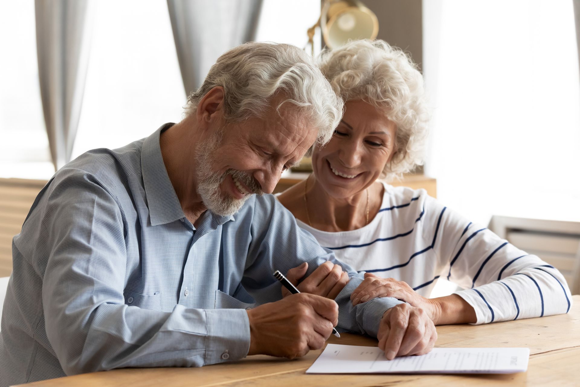 An elderly couple is sitting at a table signing a document.