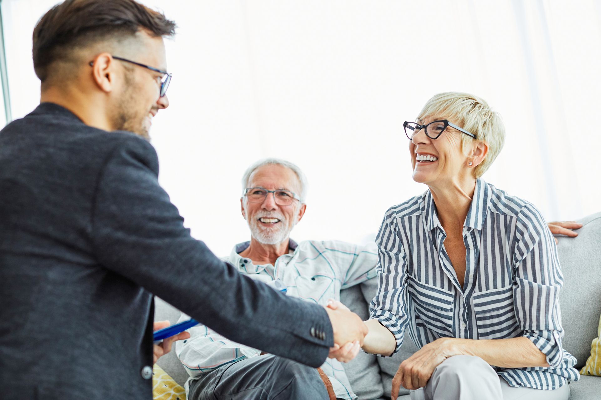 A man and woman are shaking hands while sitting on a couch.