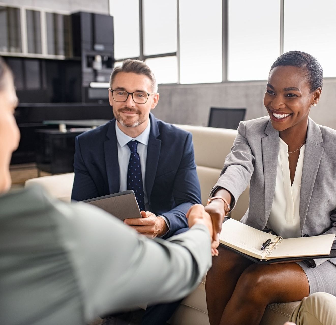 A man and a woman are shaking hands while sitting on a couch.