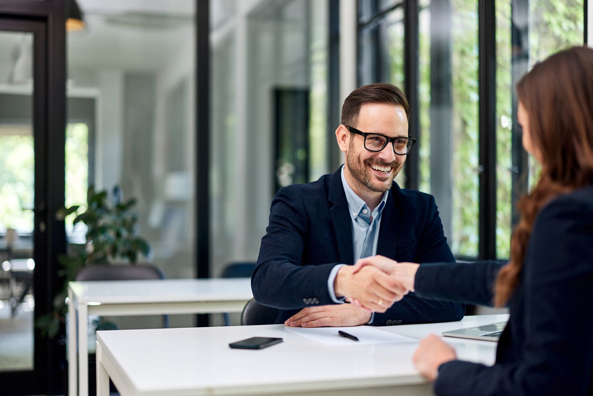 A man and a woman are shaking hands while sitting at a table.