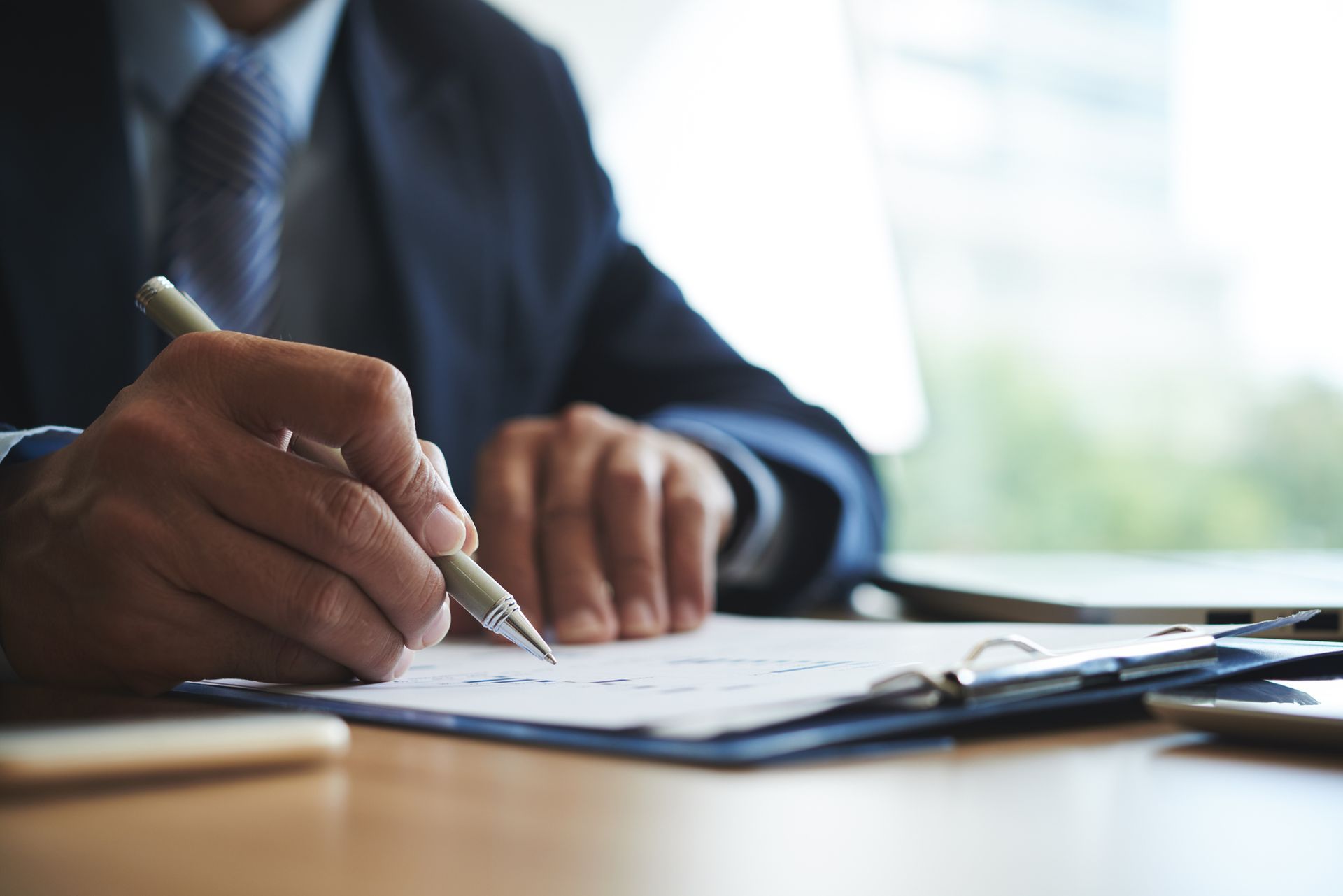 A man in a suit and tie is writing on a clipboard with a pen.