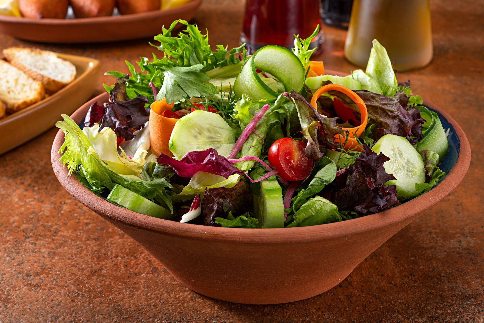 A bowl of salad with tomatoes , cucumbers , and lettuce on a table.