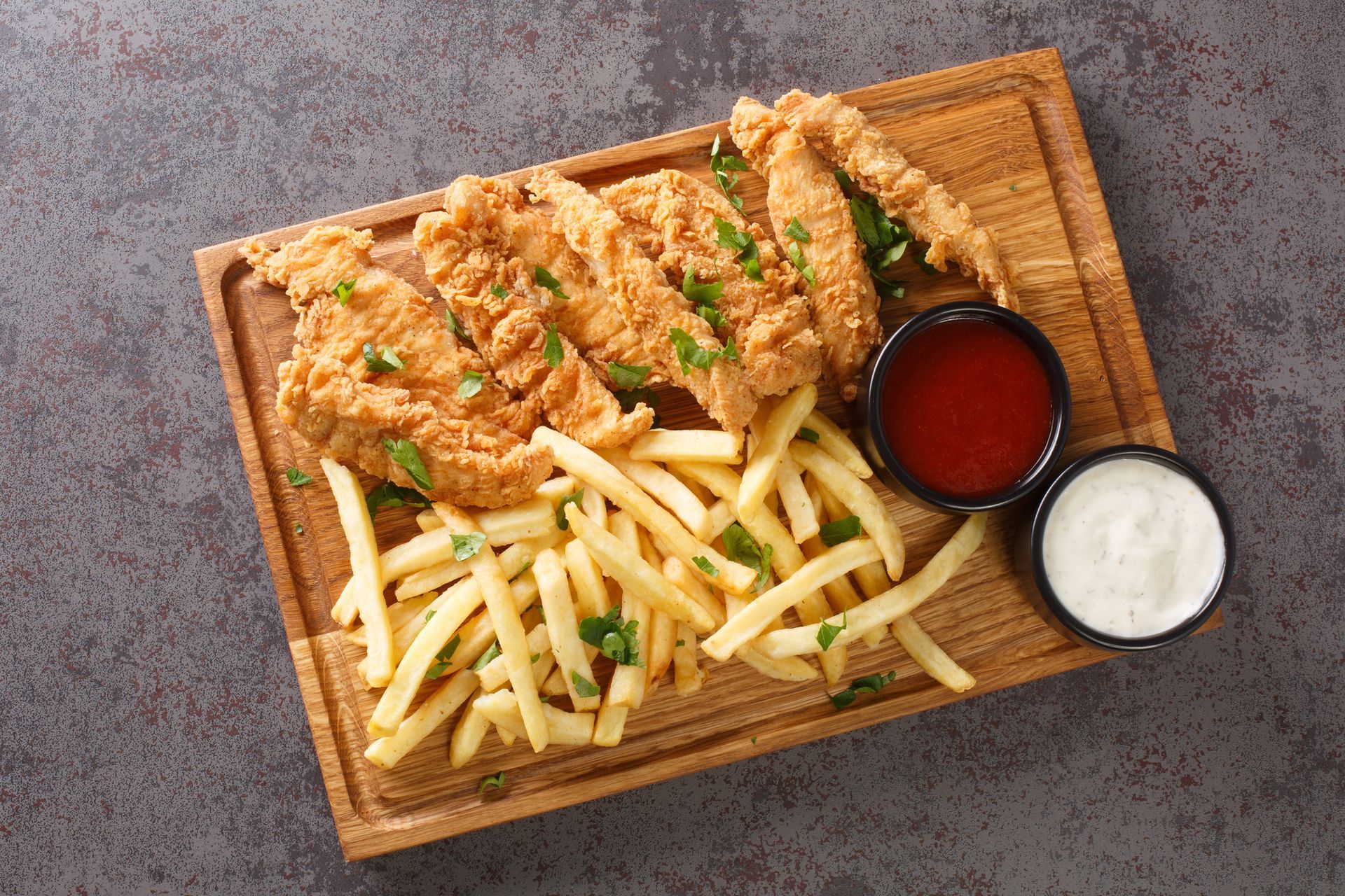 A wooden cutting board topped with fried chicken and french fries.