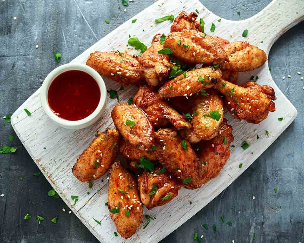 A cutting board topped with chicken wings and a bowl of ketchup.