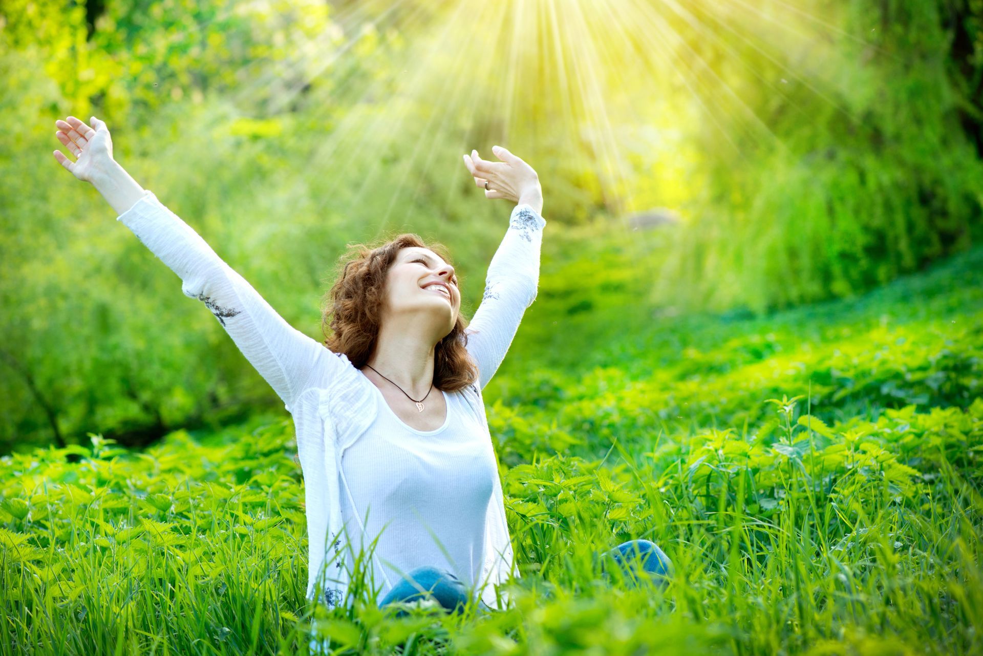 Mujer con los brazos levantados, sonriendo en un campo verde soleado.