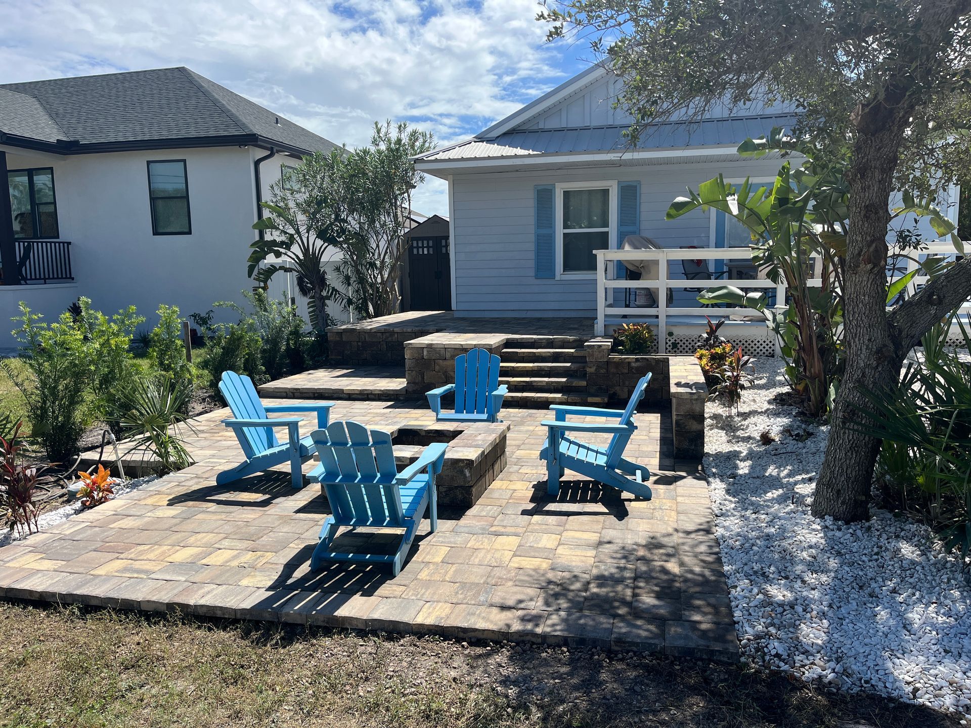 A paver patio with blue chairs and a fire pit in front of a house.