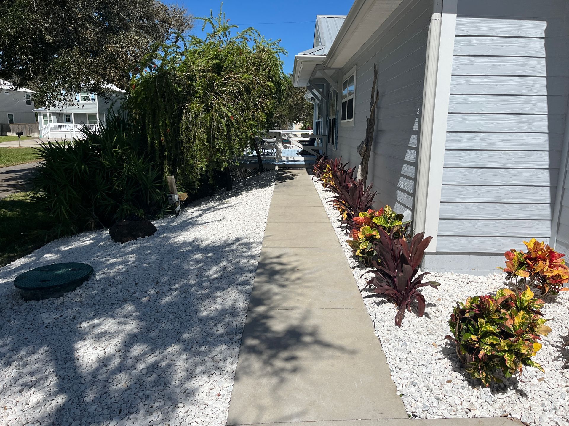A concrete sidewalk leading to a house with white gravel and flowers