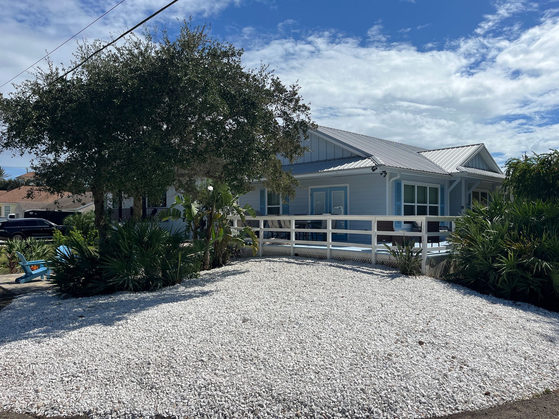 A white house with a white fence and a gravel driveway in front of it.